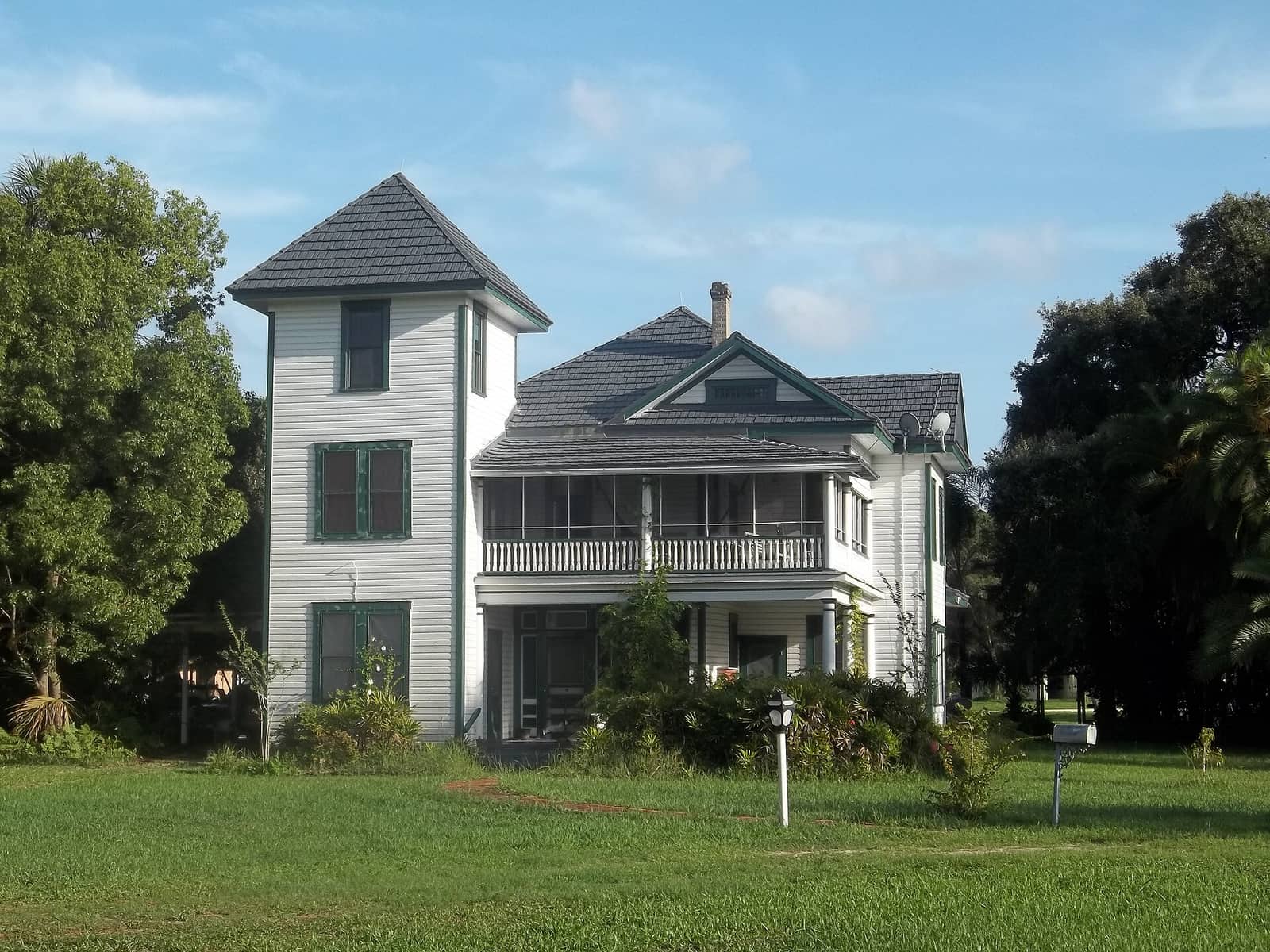 Two-storey white historic house with a screened porch, green shutters and a lawn.
