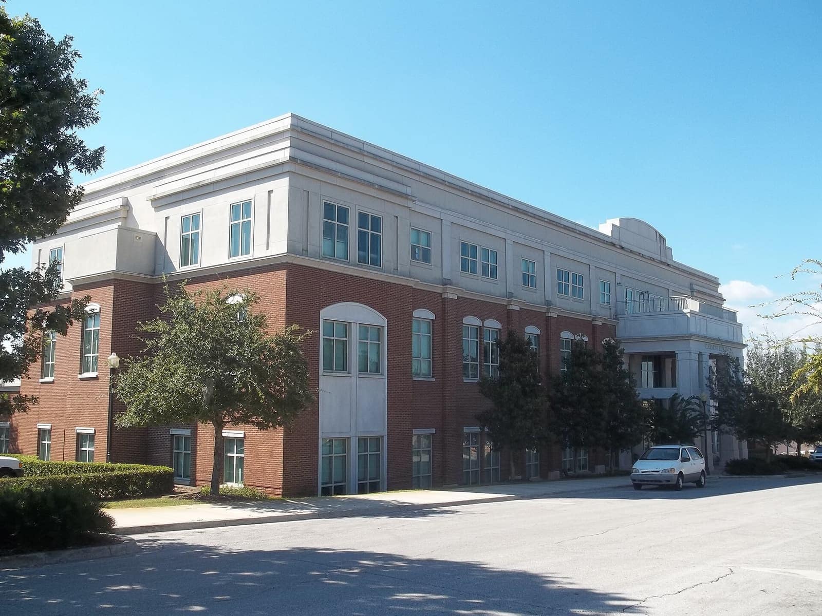 Three-story brick and cream government building with arched windows under a clear blue sky.