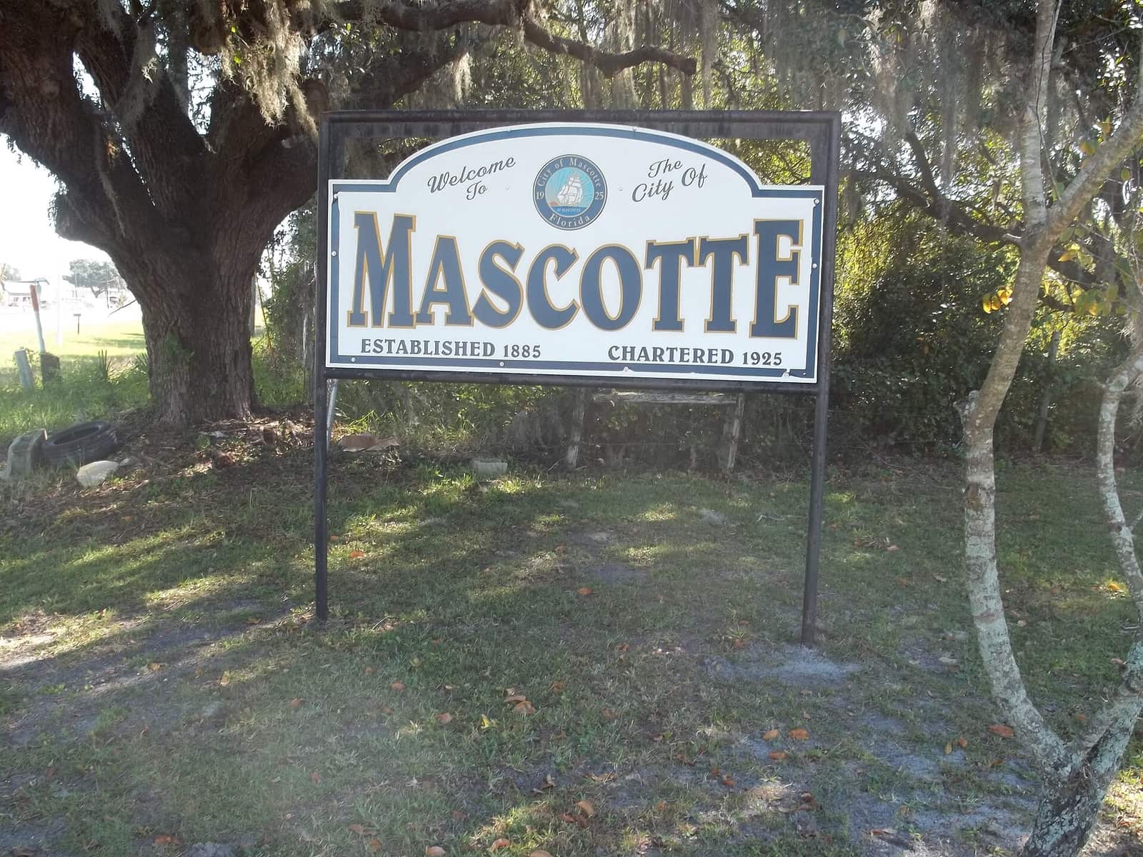 Green and white Welcome to the City of Mascotte sign standing under a large oak tree.