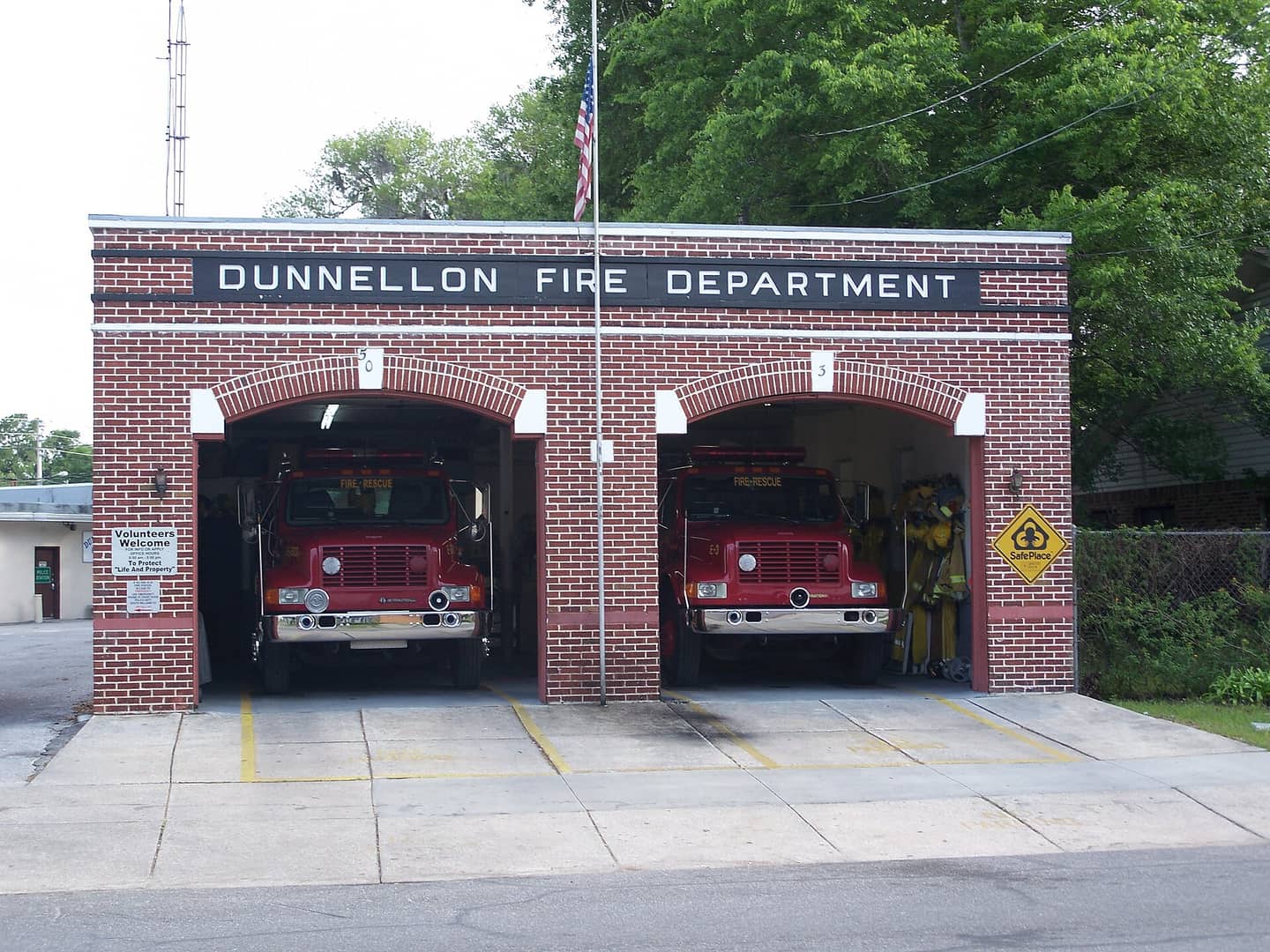 Red brick fire station with two open bays holding red fire trucks under a sign reading Dunnellon Fire Department.