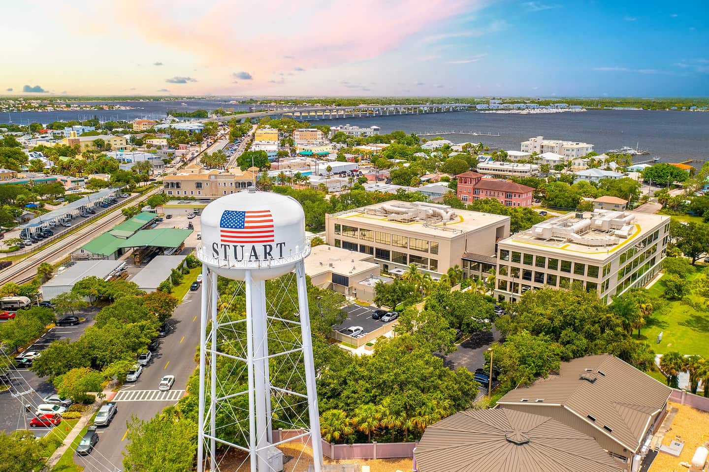 Aerial view of a water tower with a flag and STUART lettering above a town near water.
