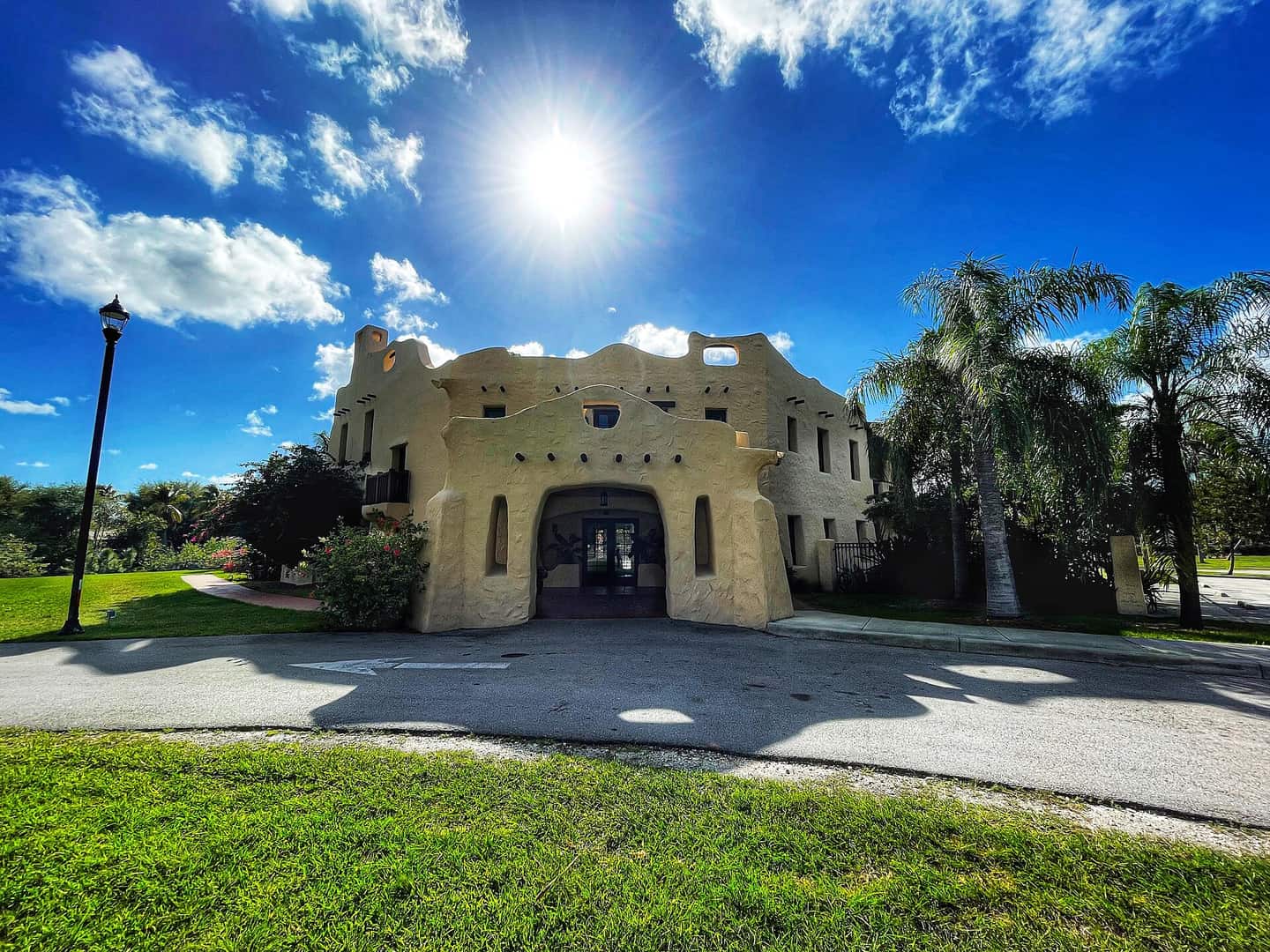 Pale stucco pueblo-style historic house with an arched entrance under a bright sun and blue sky.
