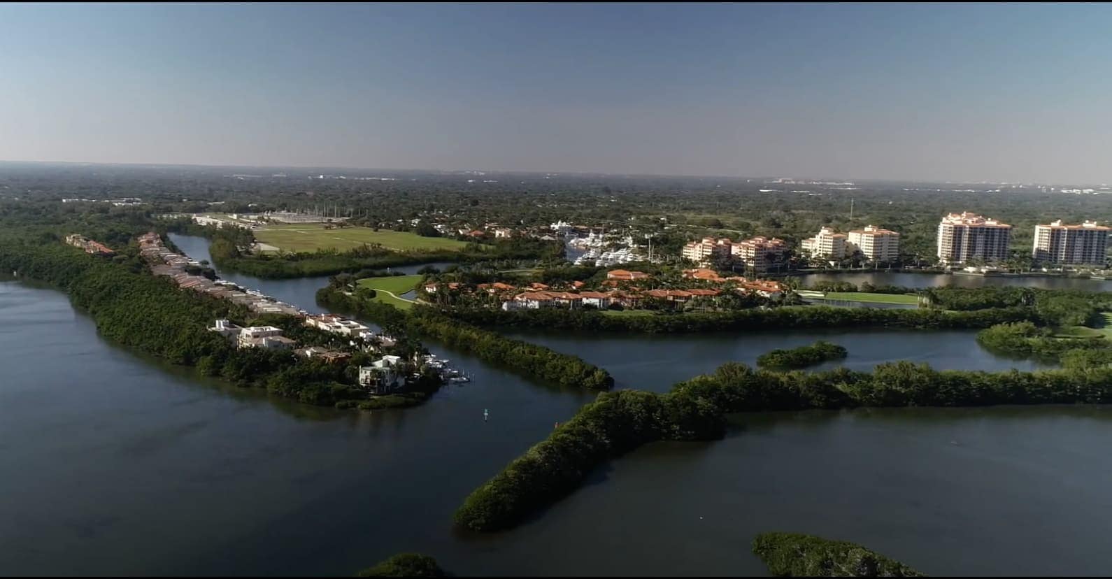 Aerial view of waterways, mangrove islands, condominium towers and green golf course under hazy sky.