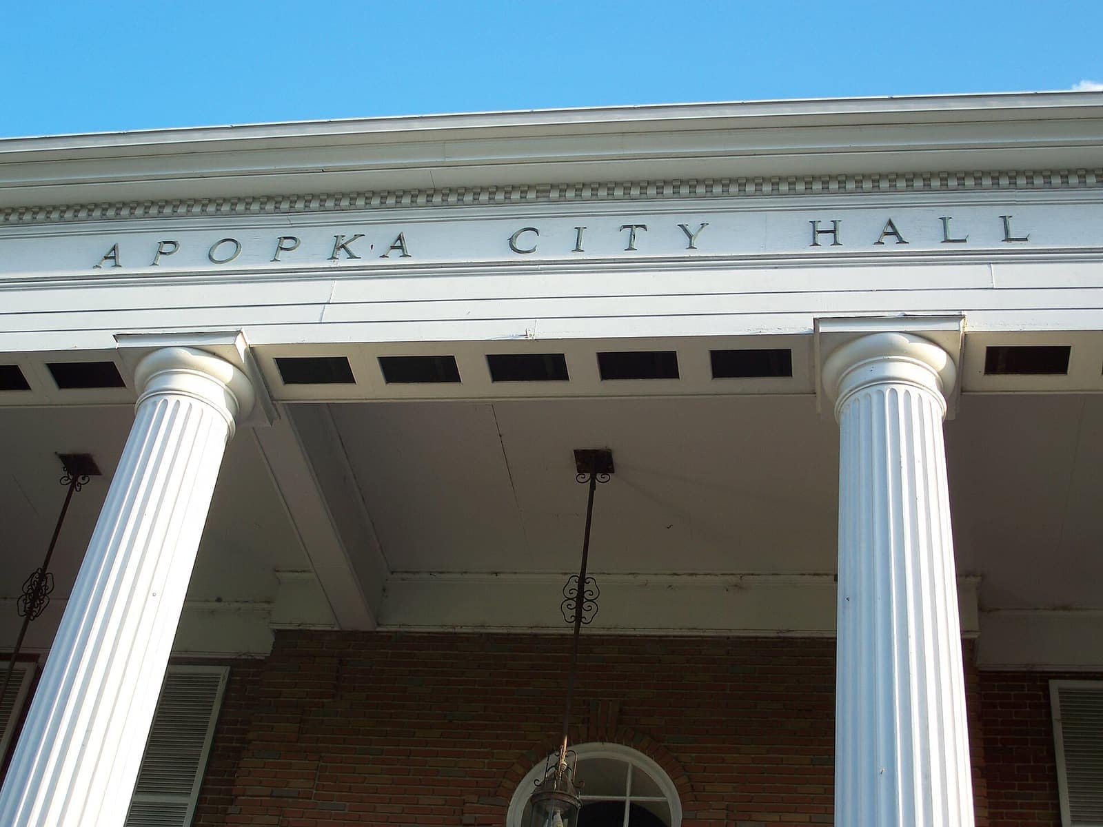 White columns and a painted cornice with the words Apopka City Hall under a clear blue sky.