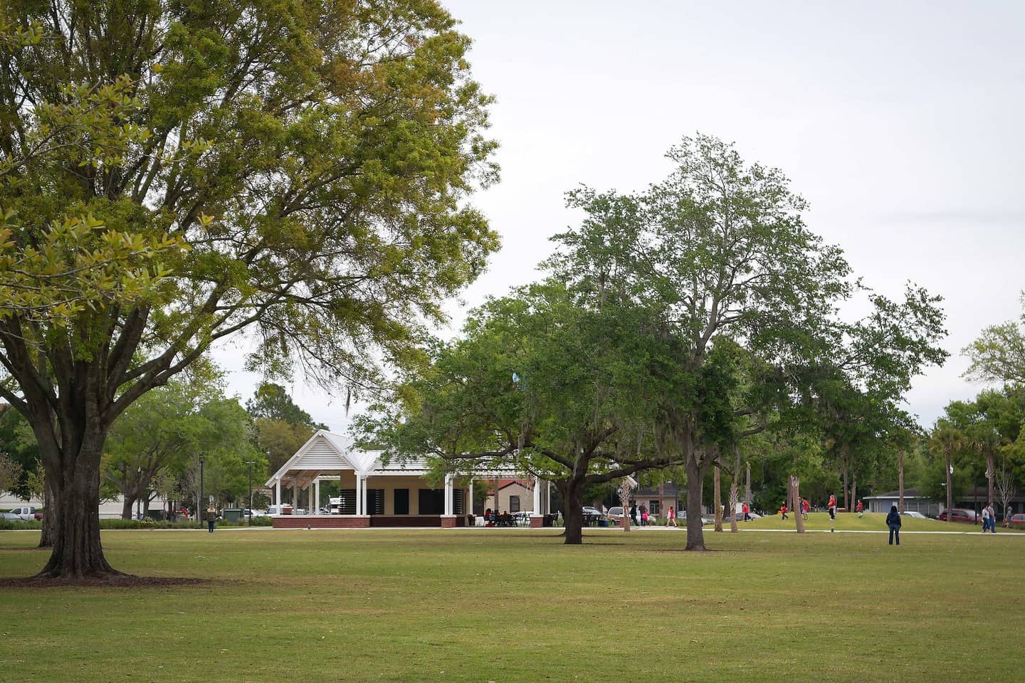 Open green lawn with large shade trees and a white gazebo pavilion under a pale overcast sky.