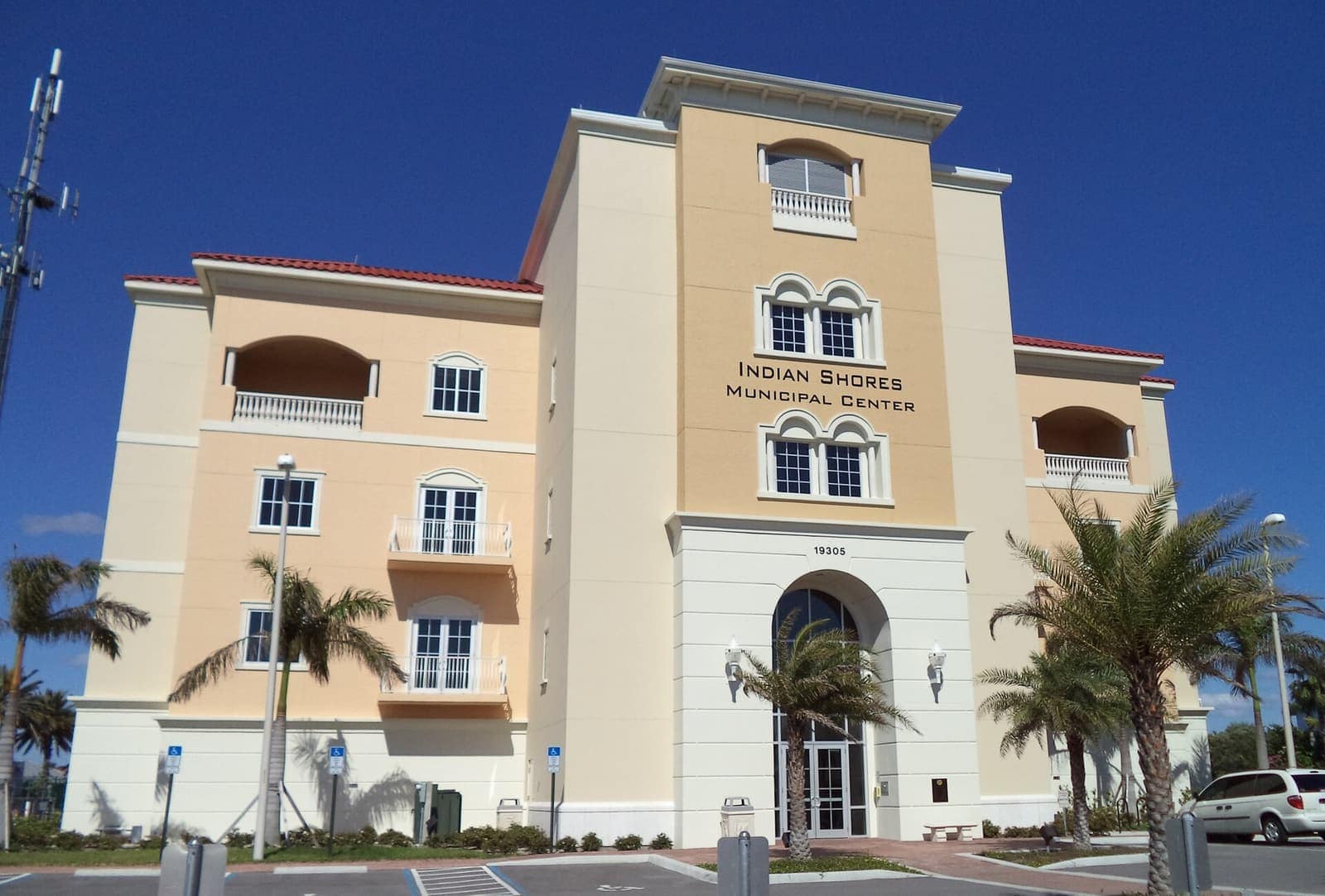 Cream-colored municipal center building with palm trees and a parking lot under blue sky.