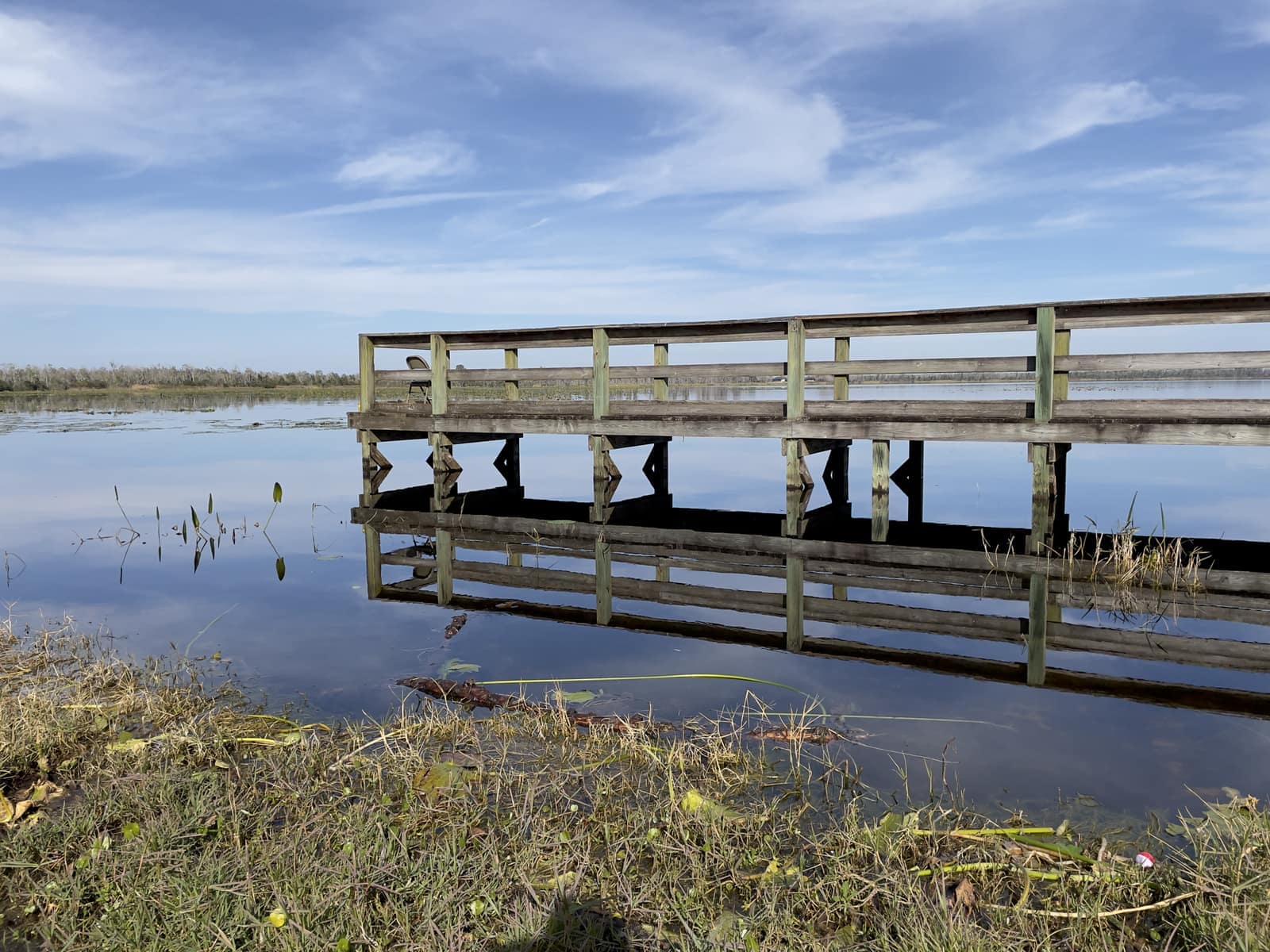 Weathered wooden boardwalk dock extends over still water under a partly cloudy sky.