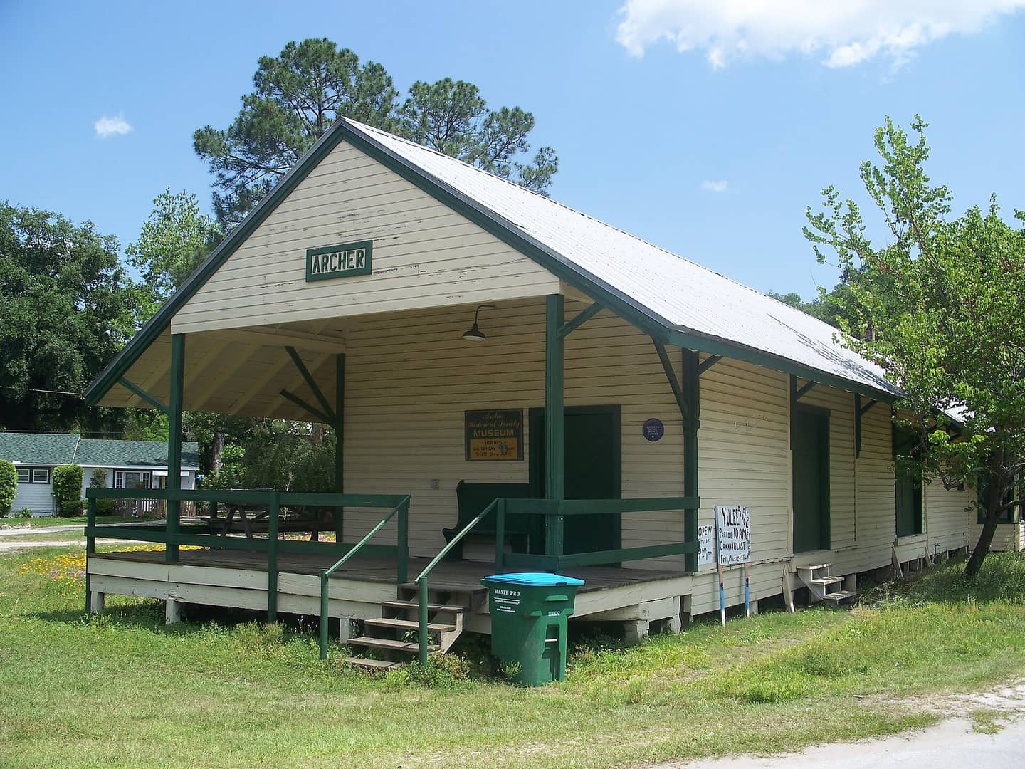 Cream wooden historical museum building with green trim, covered front porch and a sign reading Archer.