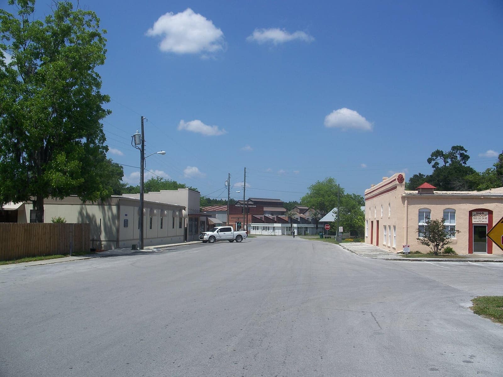 Wide two-lane main street lined with low historic storefronts and a white pickup under a bright blue sky.