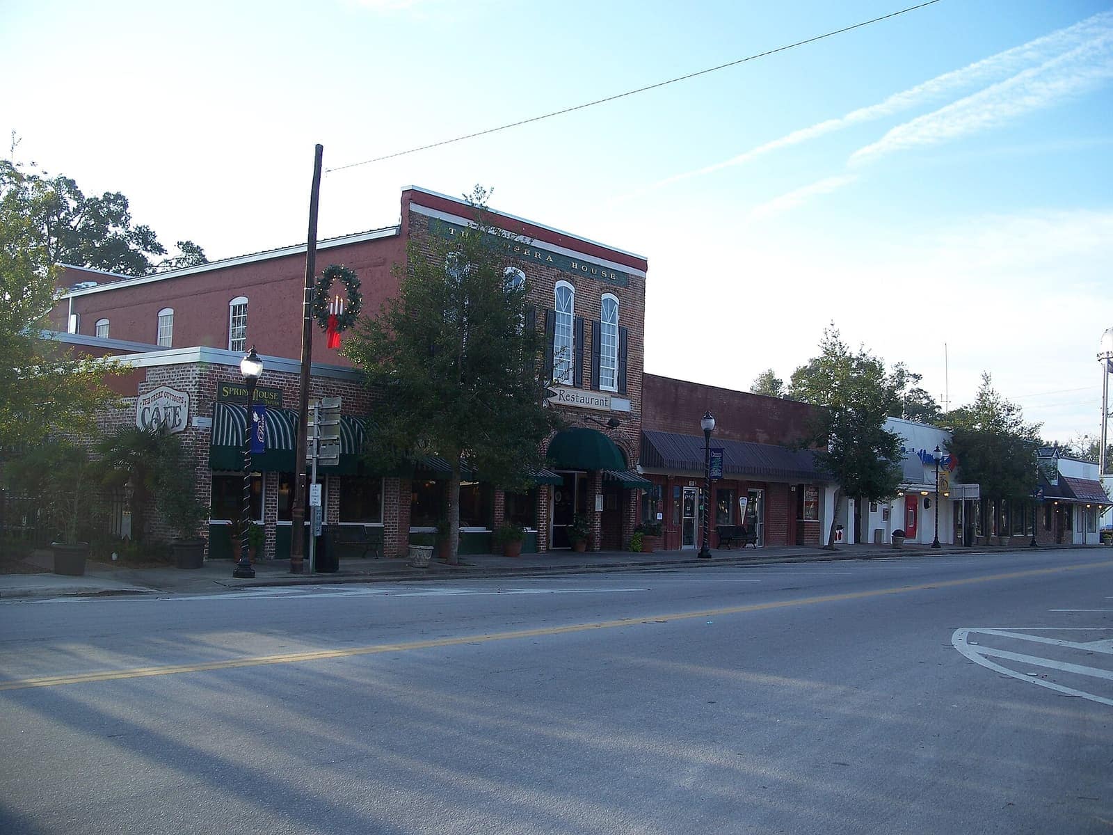 Brick downtown corner buildings with green striped awnings, a holiday wreath, and a street lamp on a sunny morning.