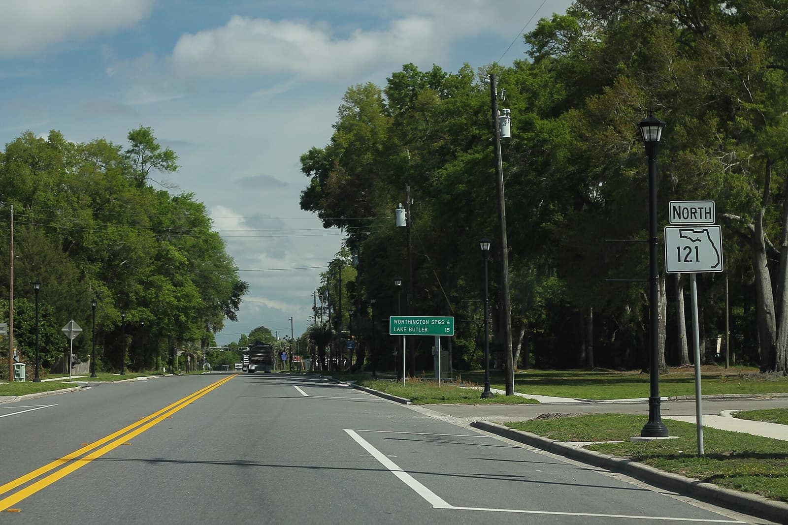 Tree-lined road with a green road sign, street lamp and a Florida route 121 north marker.