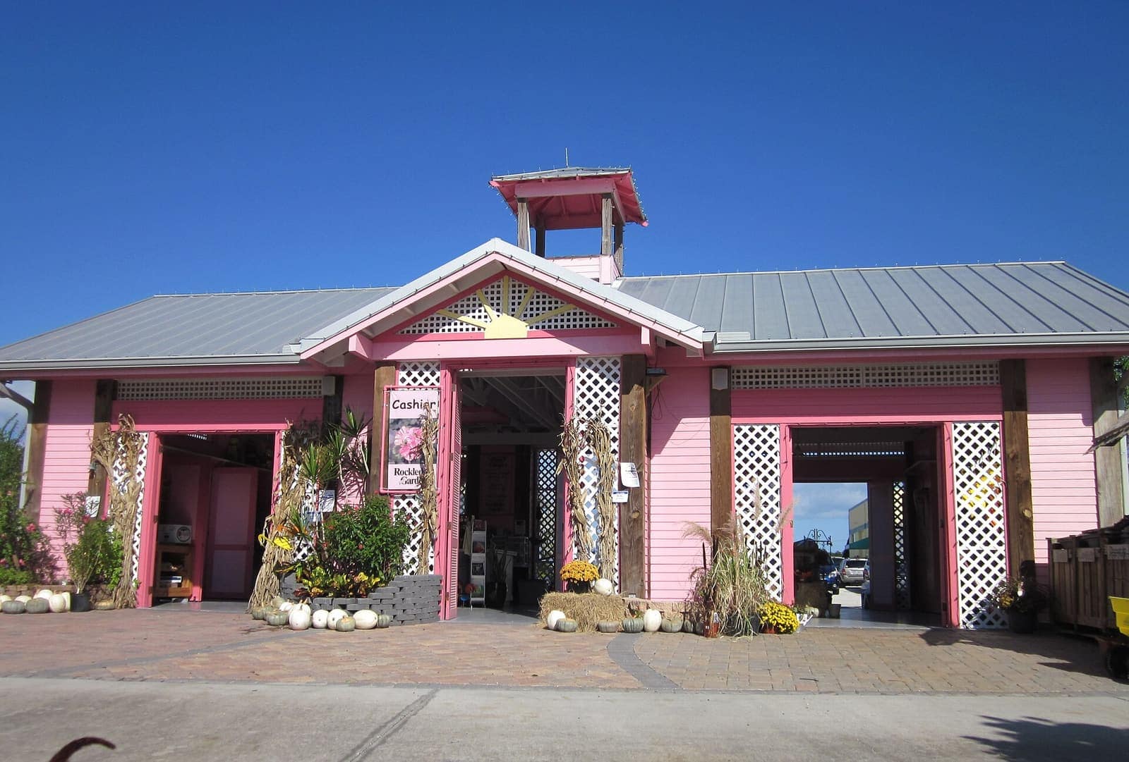 Pink garden center building with a bell tower, a metal roof and pumpkins displayed under a clear blue sky.