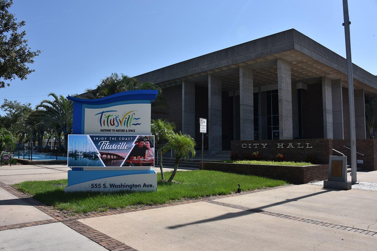 Modern concrete city hall building with columns, a welcome sign, and palm trees along the walkway.