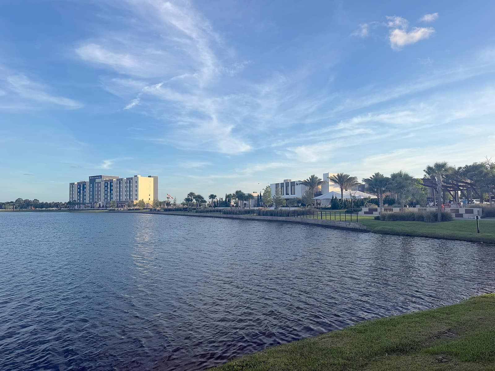 Calm lake with a yellow high-rise hotel and white buildings under a blue sky.