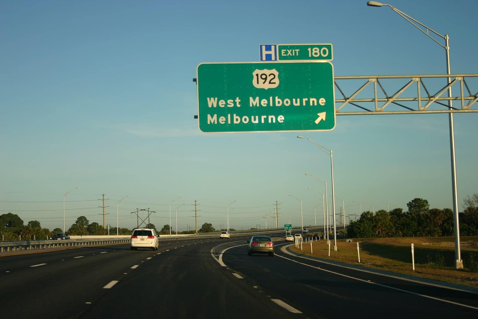 Green interstate exit sign showing US 192 to West Melbourne and Melbourne above a sunny divided highway.