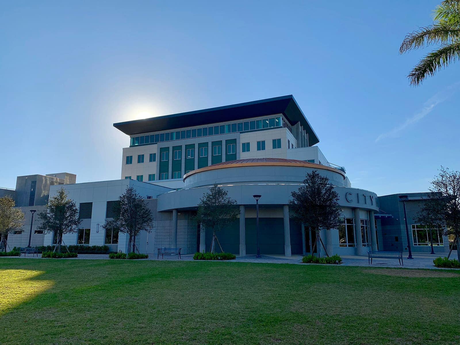 Modern multi-storey city hall building with a curved front and lawn under a clear blue sky.