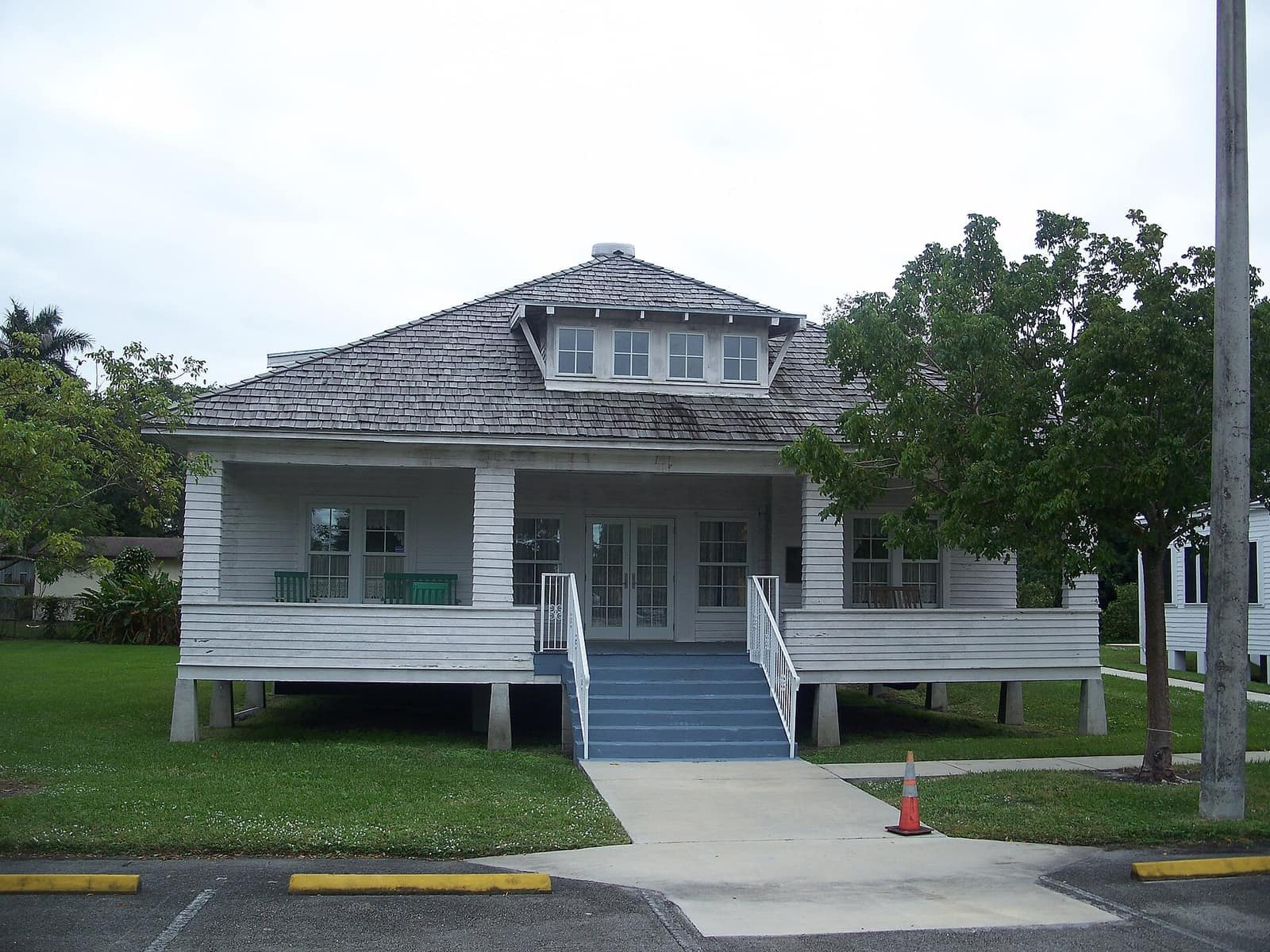 White wooden historic house with a covered front porch, steps, and a shingled roof on a lawn.