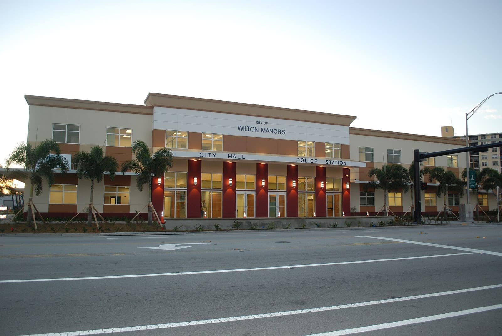 Two-story city hall building with palm trees, a traffic signal, and an empty street in the foreground.