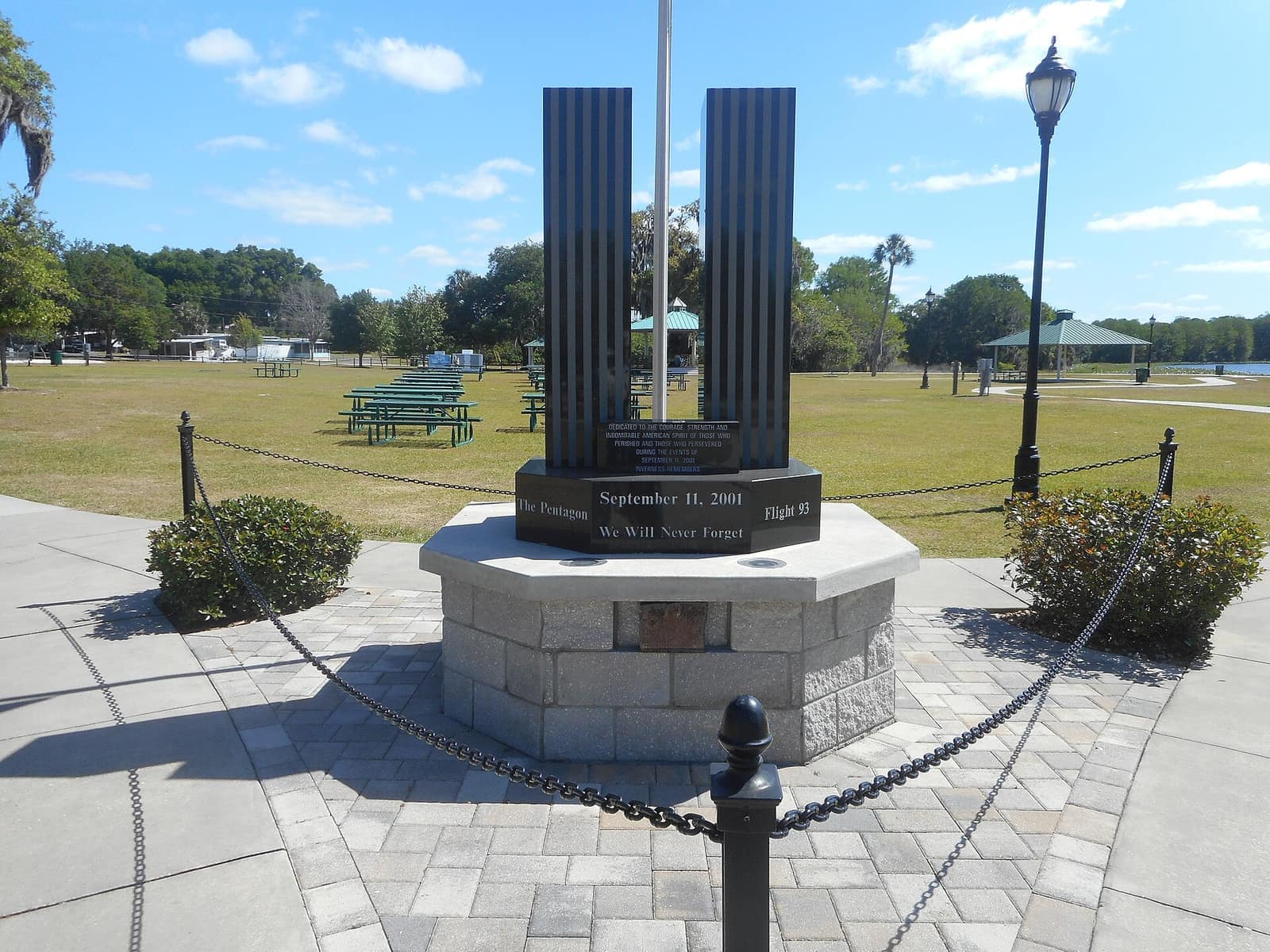 Granite September 11 memorial with two dark steel panels on a circular base in a sunny park.