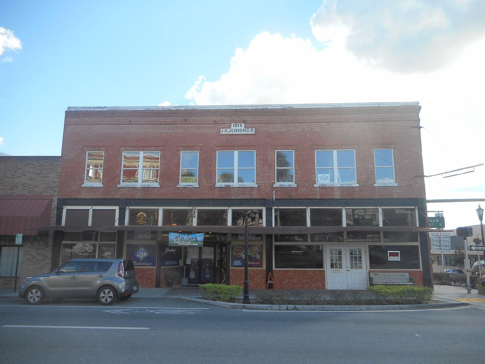 Two-story 1915 brick commercial building with storefronts on a sunny street corner.