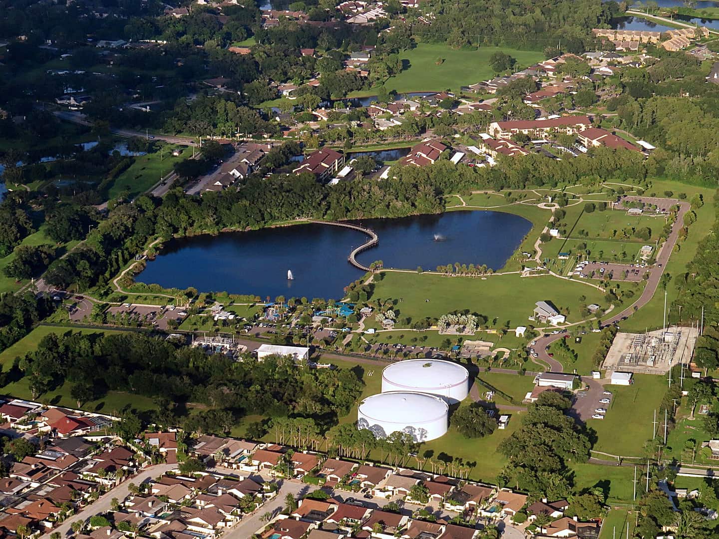 Aerial view of a lake with sailboats, green park grounds, and surrounding residential neighborhoods.