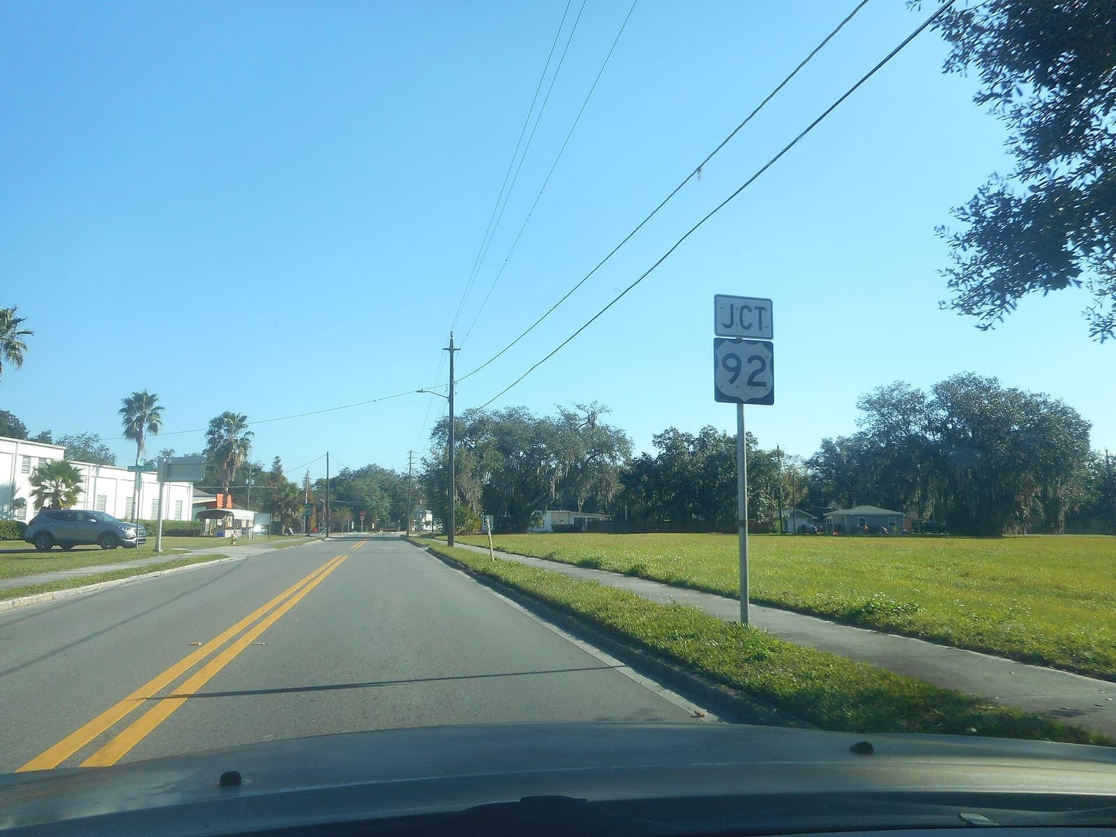 Two-lane road with yellow center lines runs toward a JCT US 92 route sign under a clear blue sky.