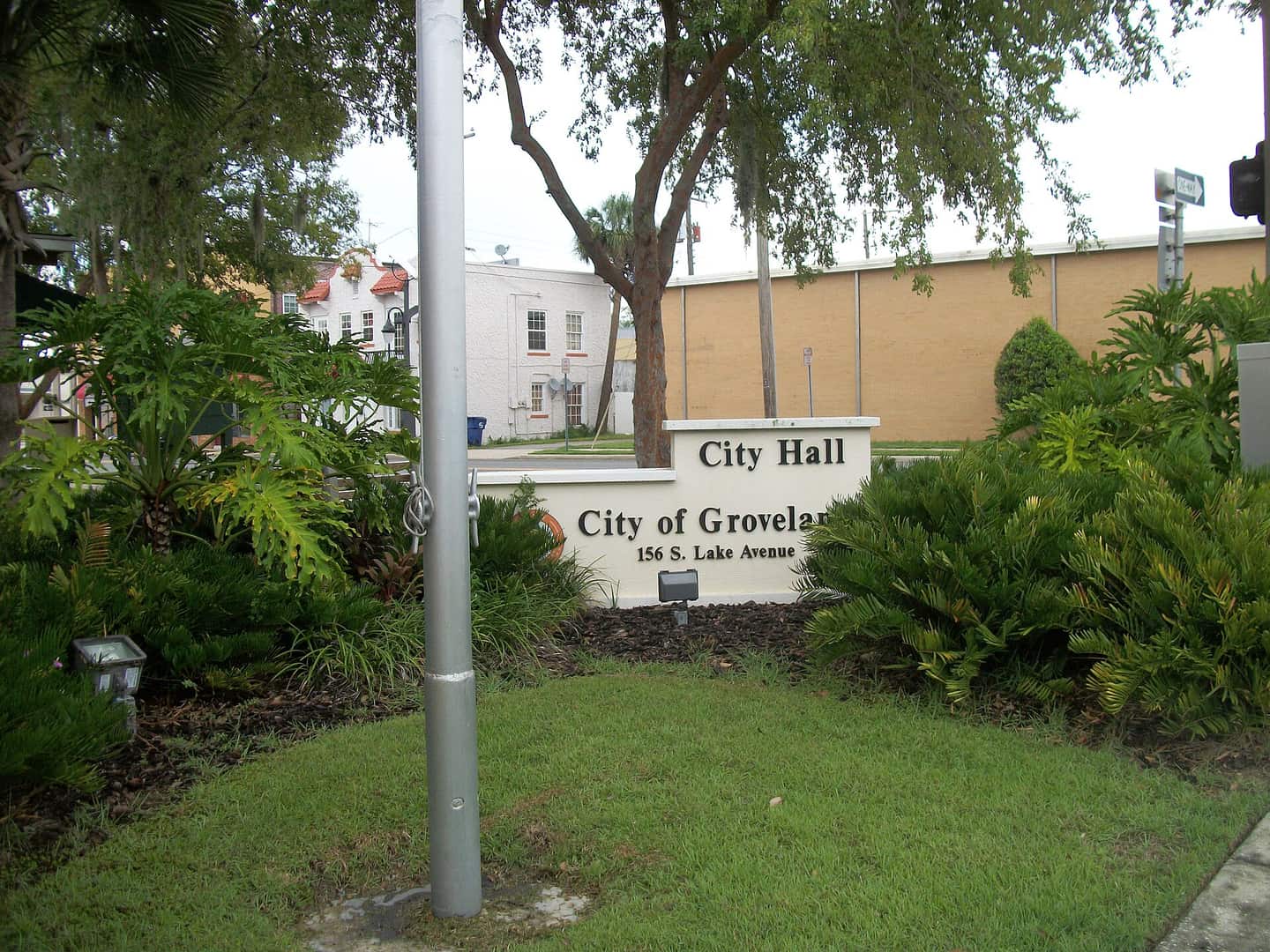 Green City of Groveland sign with City Hall lettering in front of shrubs and a large tree.
