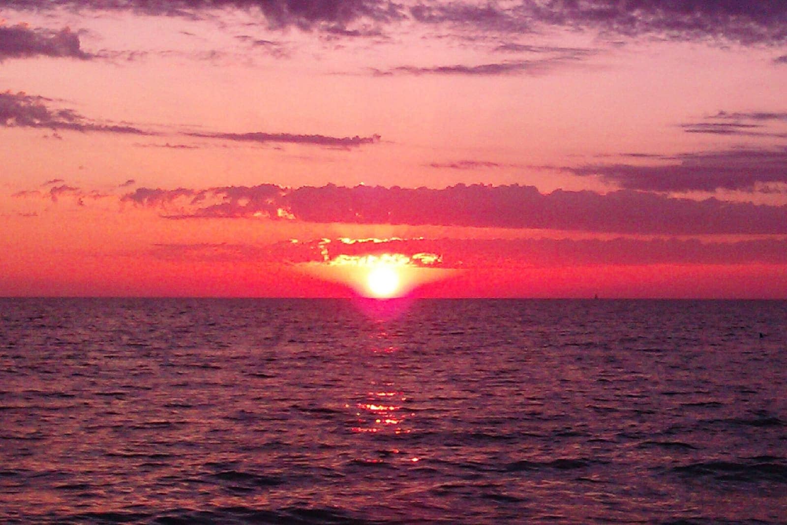 Sun setting over calm open water under pink and orange clouds.