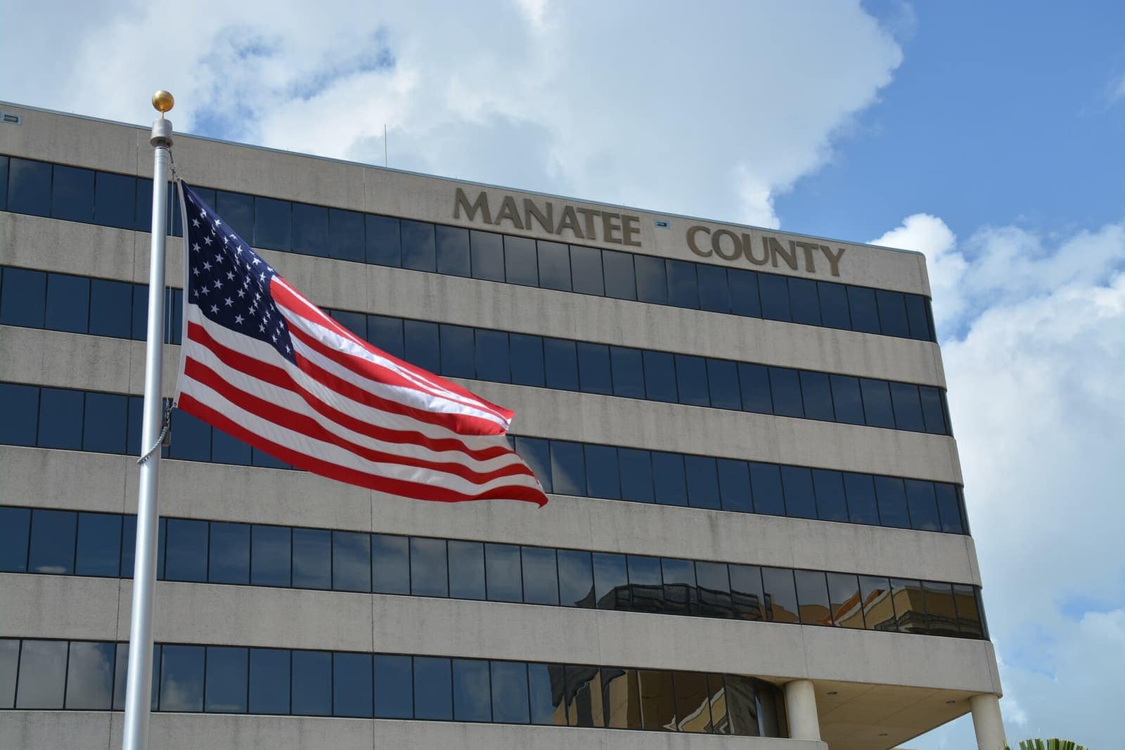Multi-story government office building with a large American flag and the words MANATEE COUNTY on its facade.