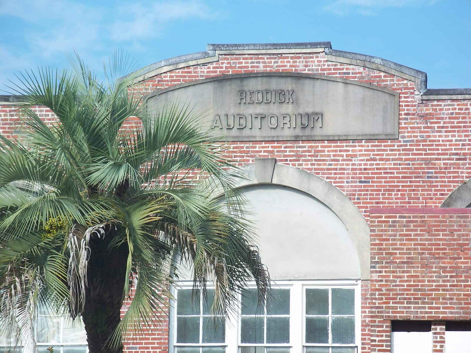 Brick facade with carved stone sign reading Reddick Auditorium, with a palm tree in front.