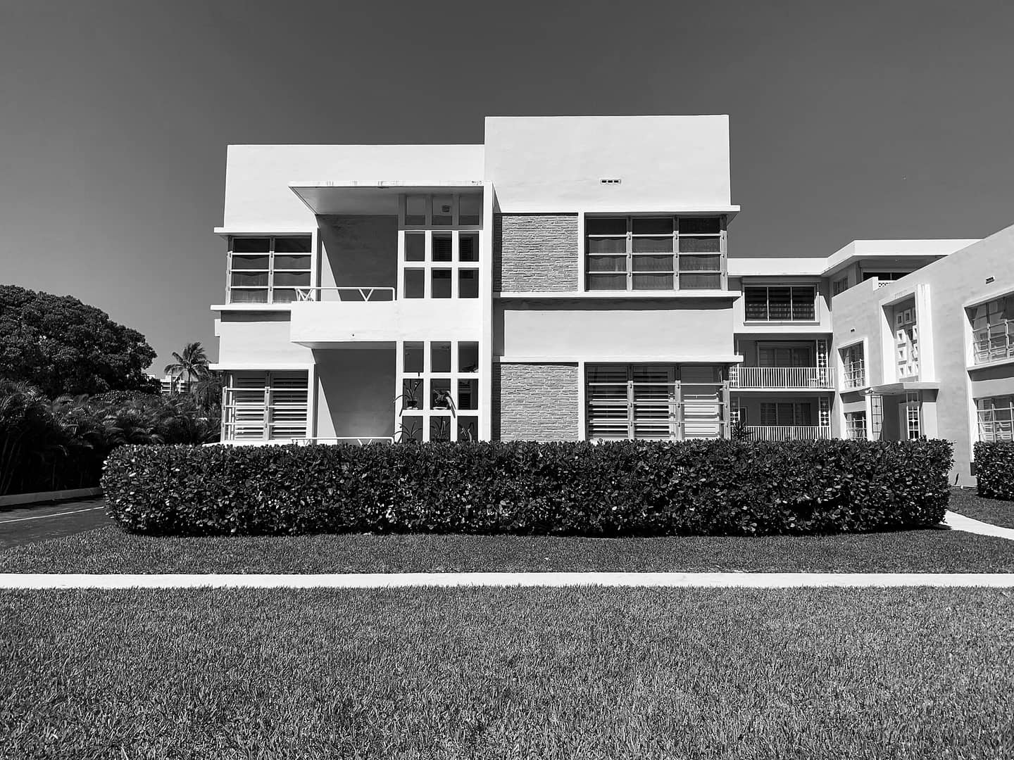 Black-and-white photo of a two-storey midcentury apartment building with a clipped hedge and lawn.