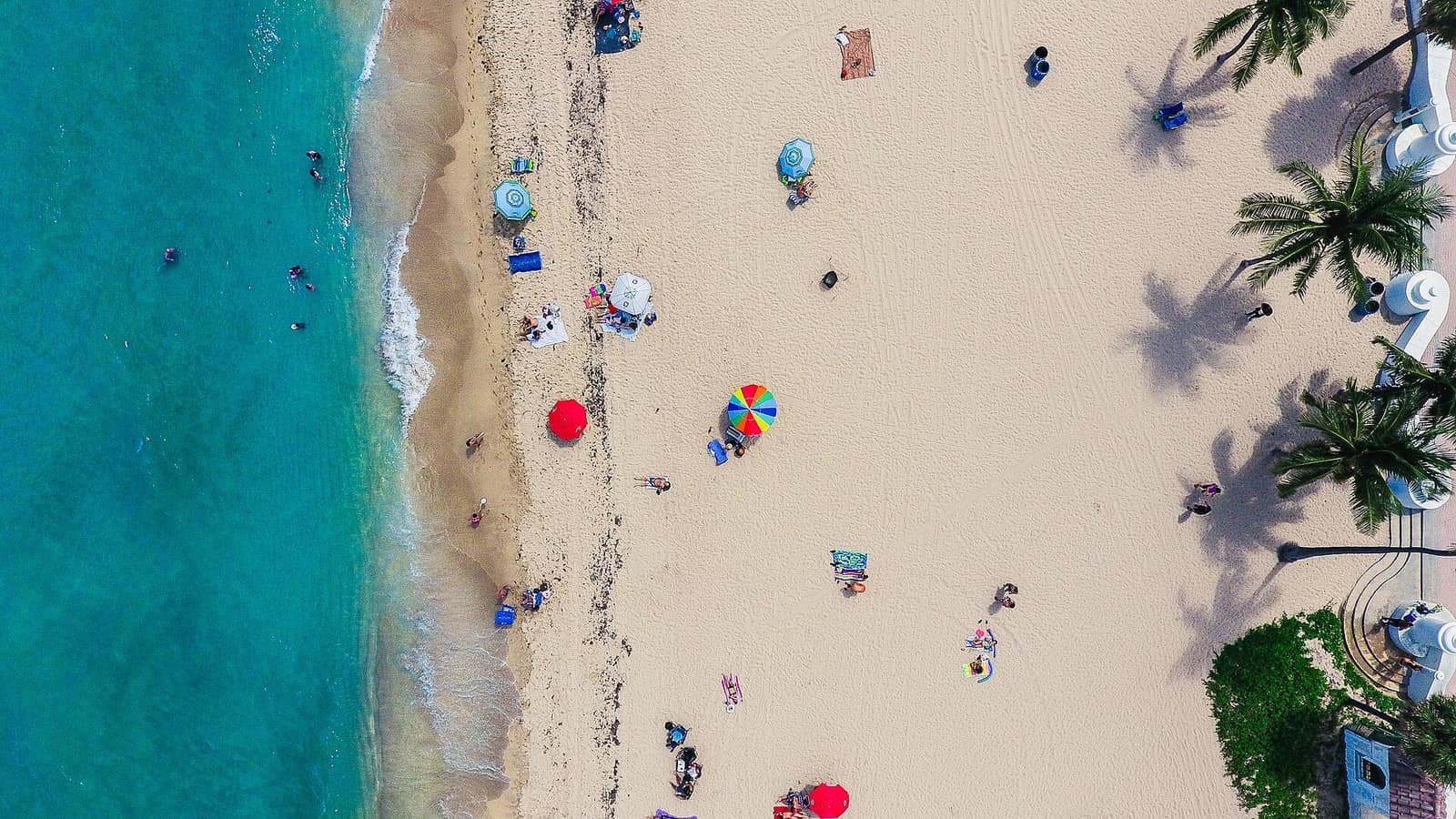 Overhead view of sandy beach with turquoise water, umbrellas and small scattered people.