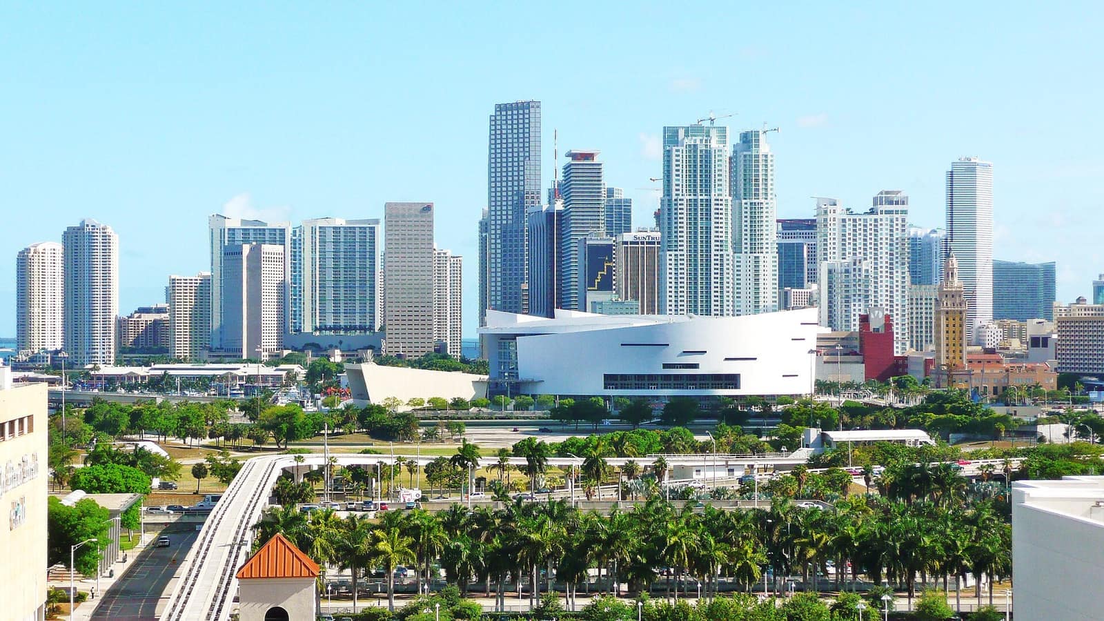 Downtown towers and a white modern museum building behind a row of palm trees on a sunny day.