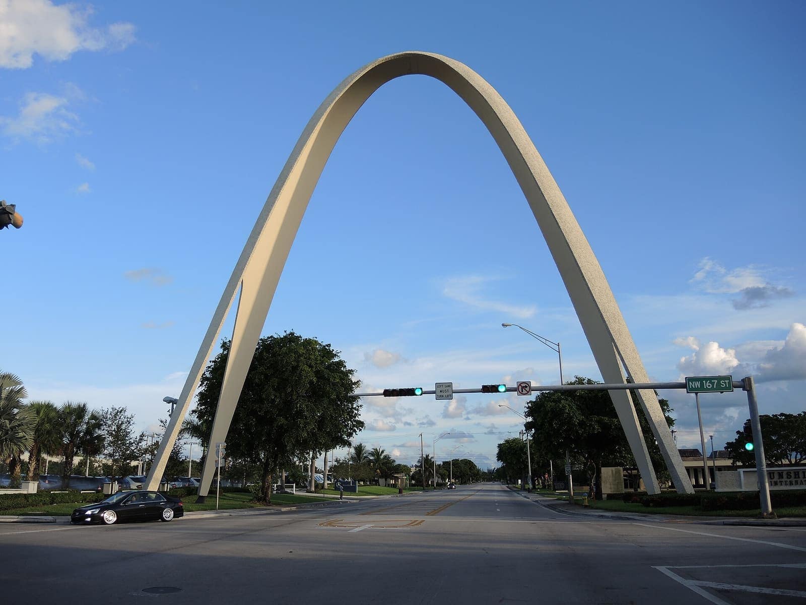 Curved concrete arch rises above a wide, empty boulevard with traffic signals and a single distant car.