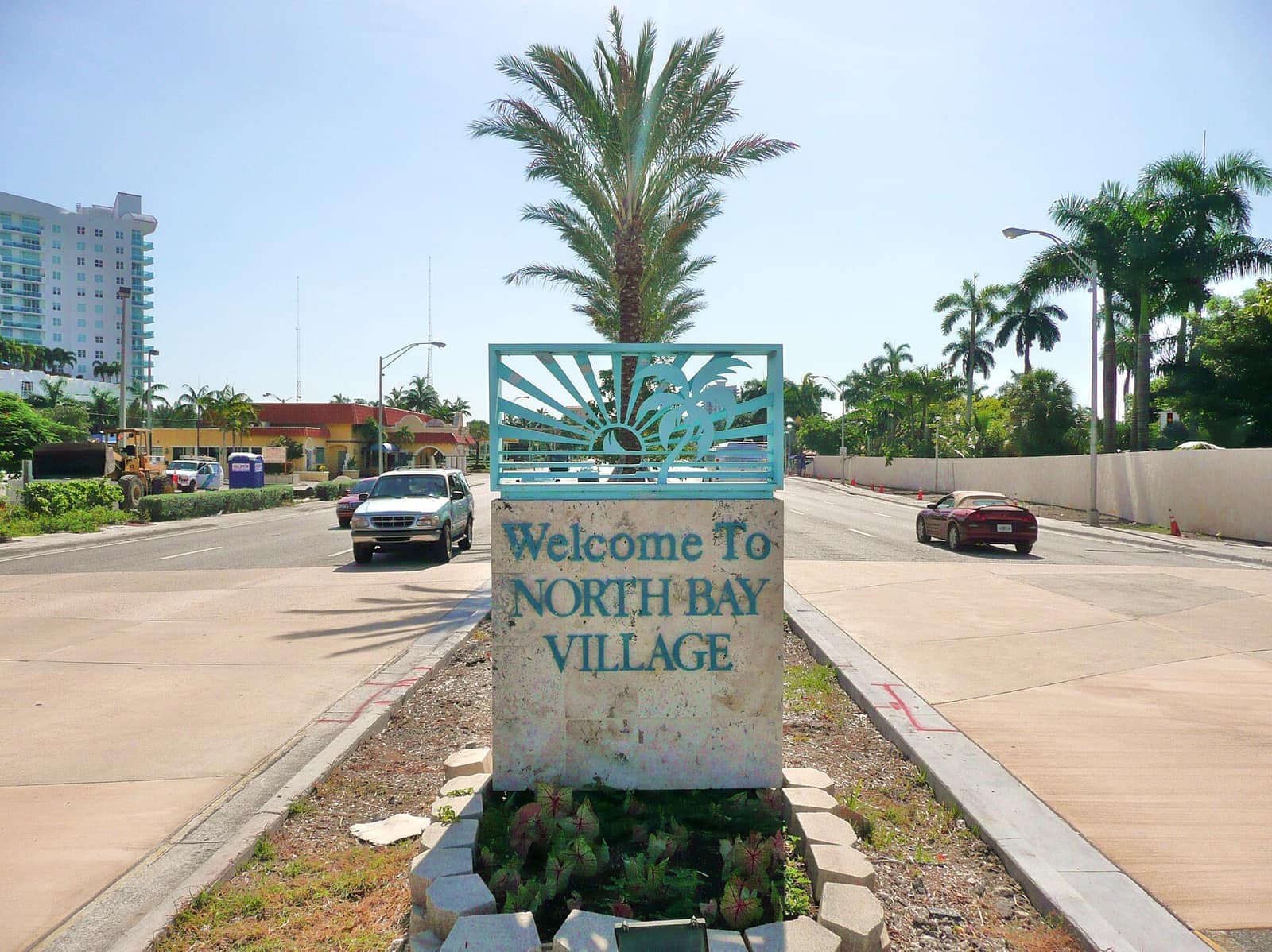 Teal Welcome to North Bay Village sign with palm tree on a divided street.
