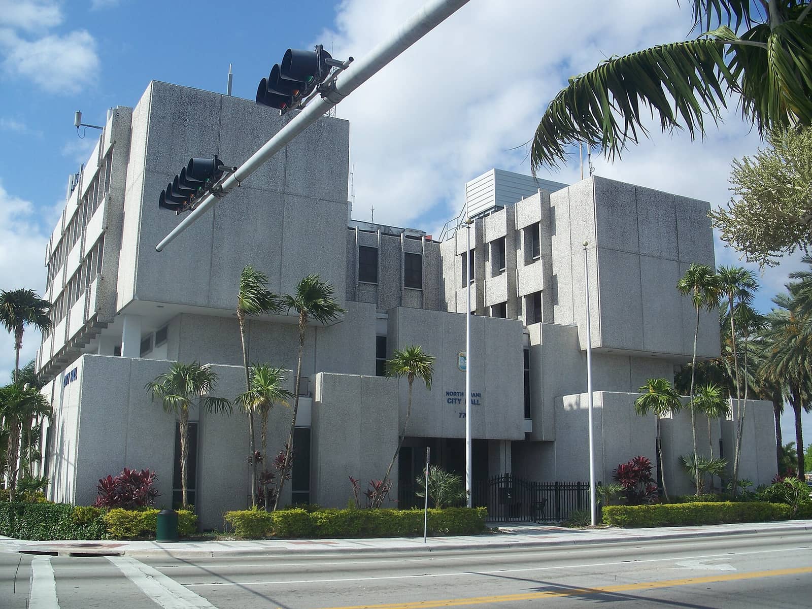 Gray concrete modernist government building with palm trees and a traffic signal arm in the foreground.