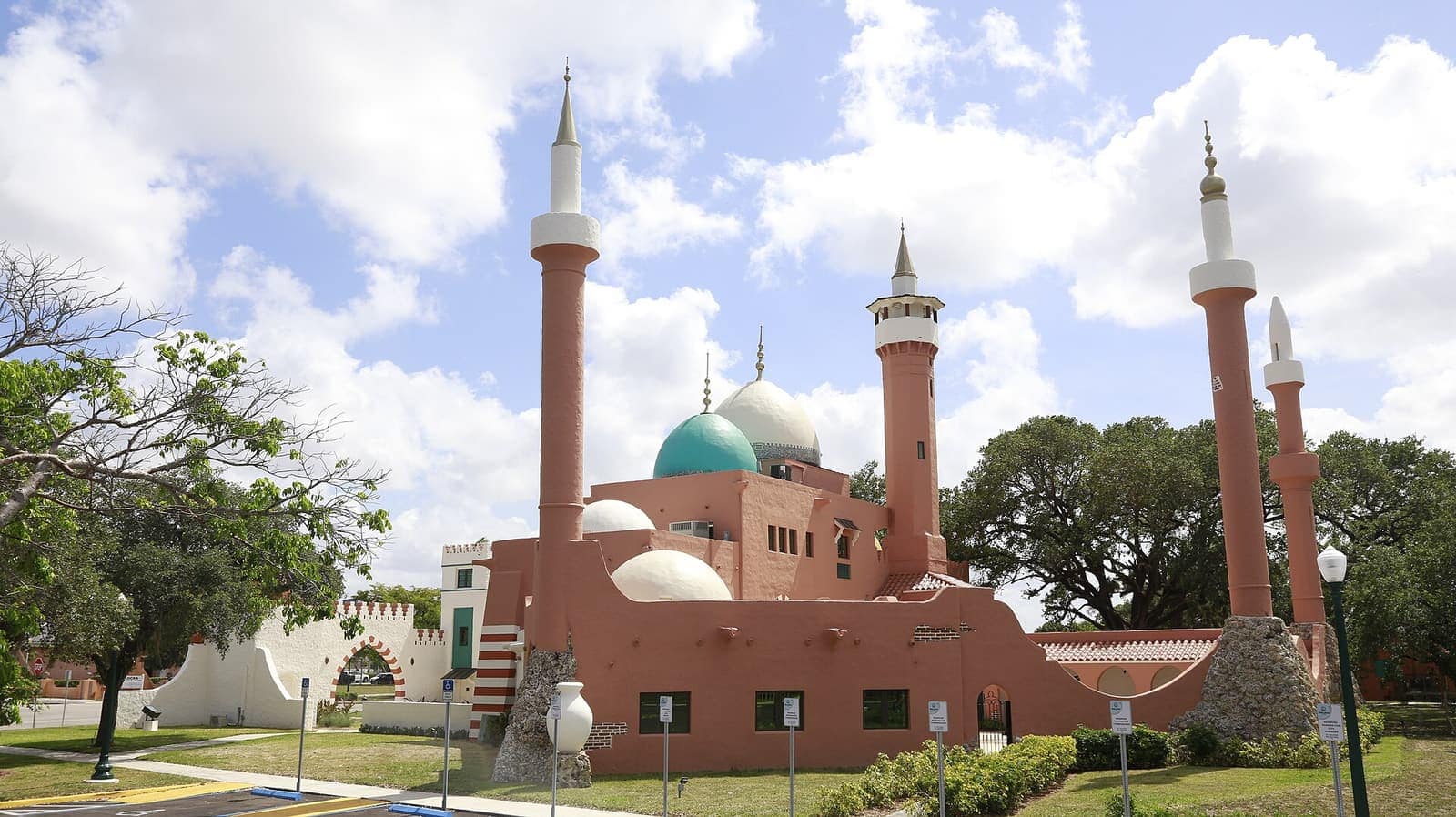 Pink domed Moorish-style building with minarets and a green dome under a partly cloudy blue sky.