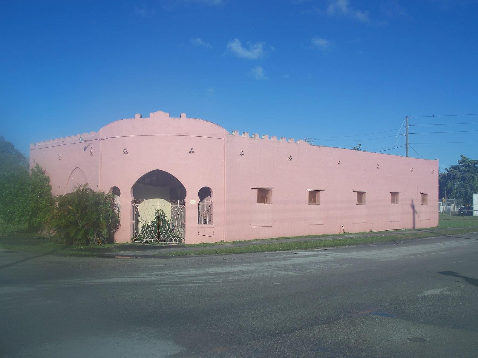 Pink Moorish-style showroom building with arched entrance and crenellated walls under a clear blue sky.