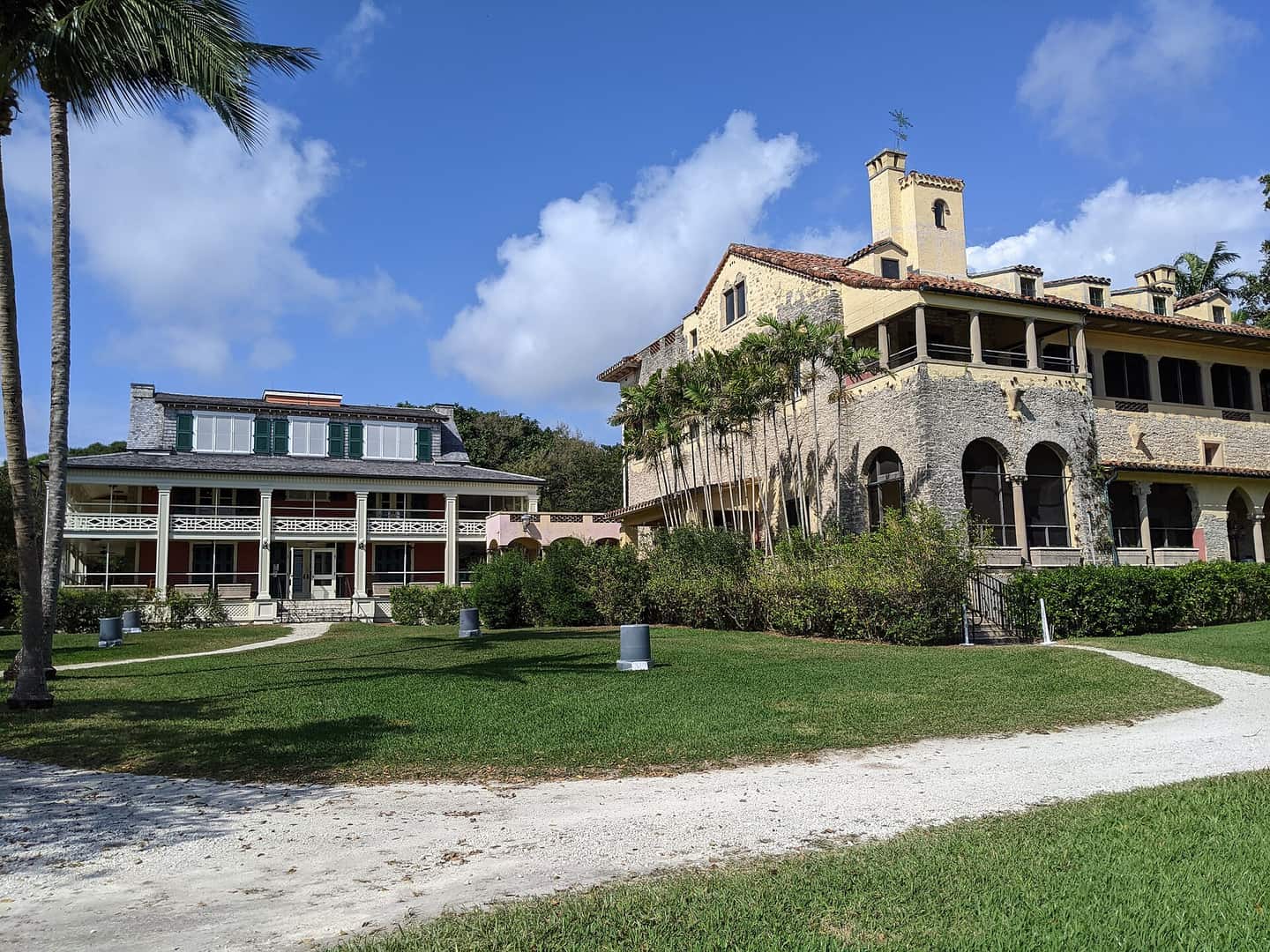 Two historic stone and stucco mansions with arched windows and lawns beneath a blue sky with clouds.