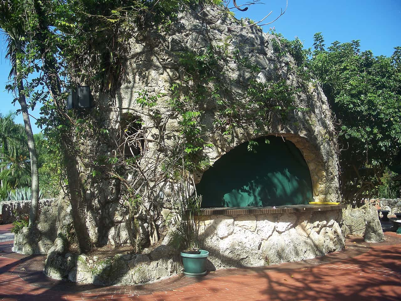 Ivy-covered coral stone concession stand with a green arched opening beside a red brick plaza.