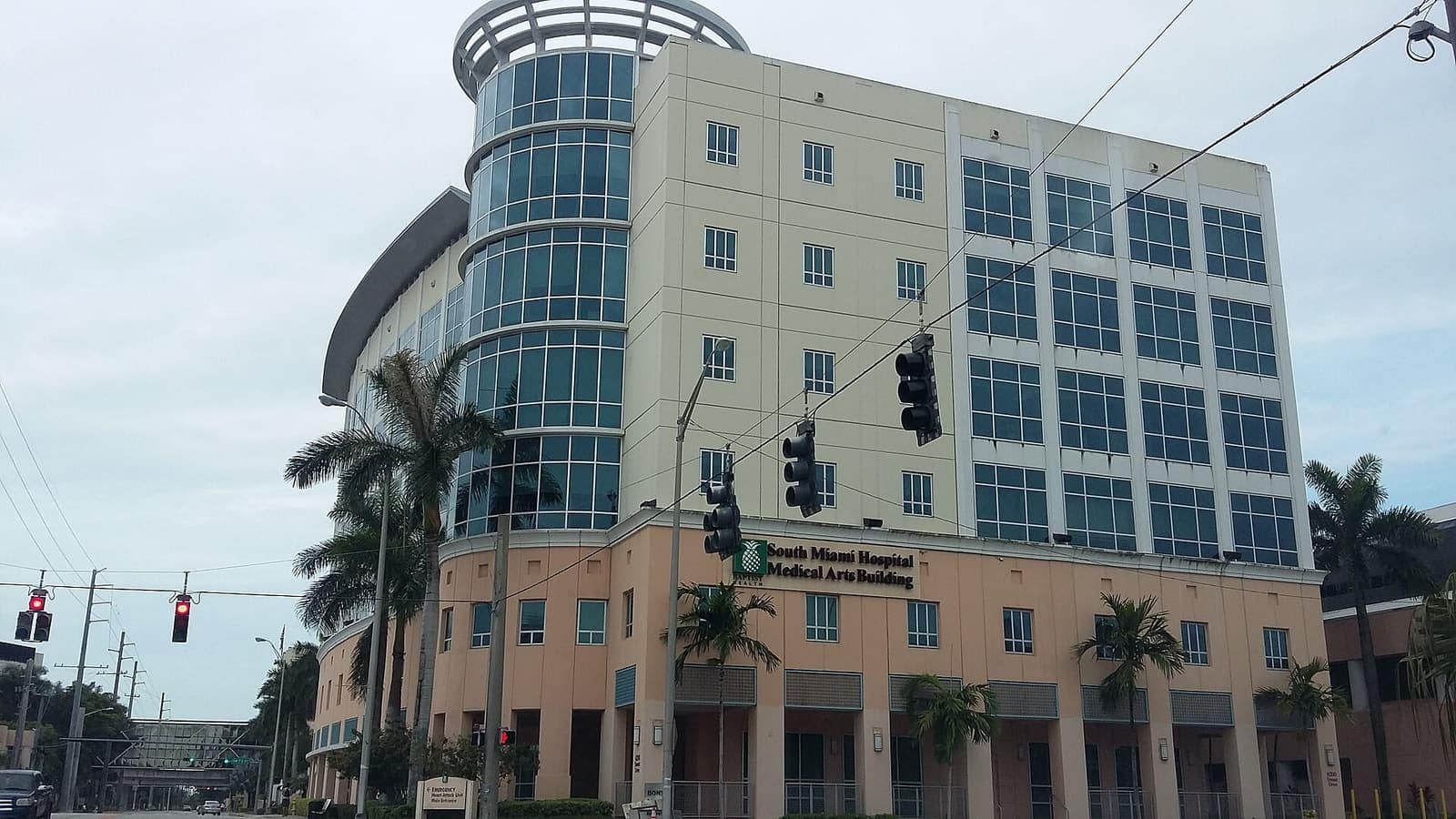 Five-story cream medical office building with a curved glass tower and palm trees beside a city street.