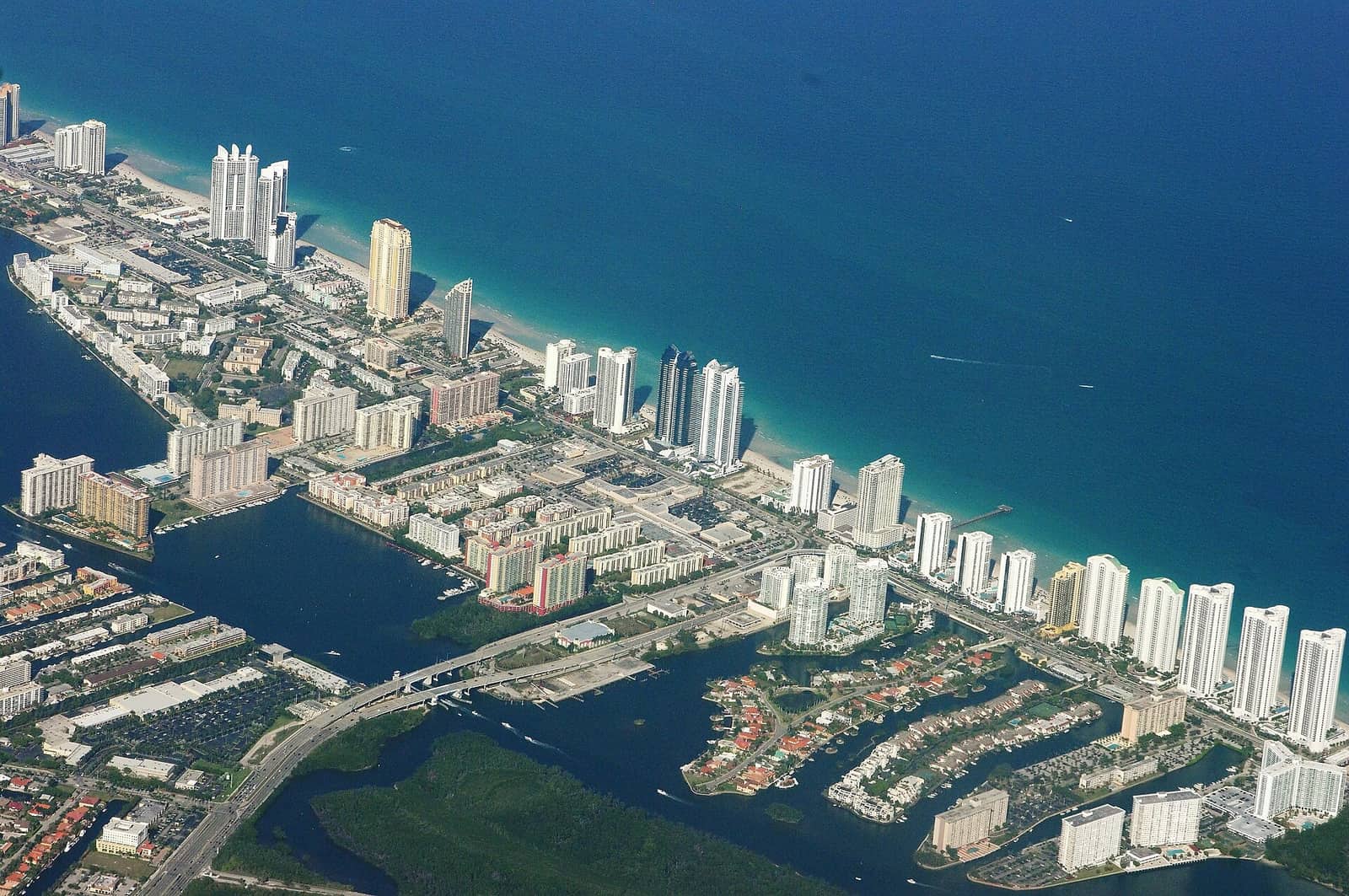 Aerial view of high-rise towers, waterways and coastline beside deep blue ocean.