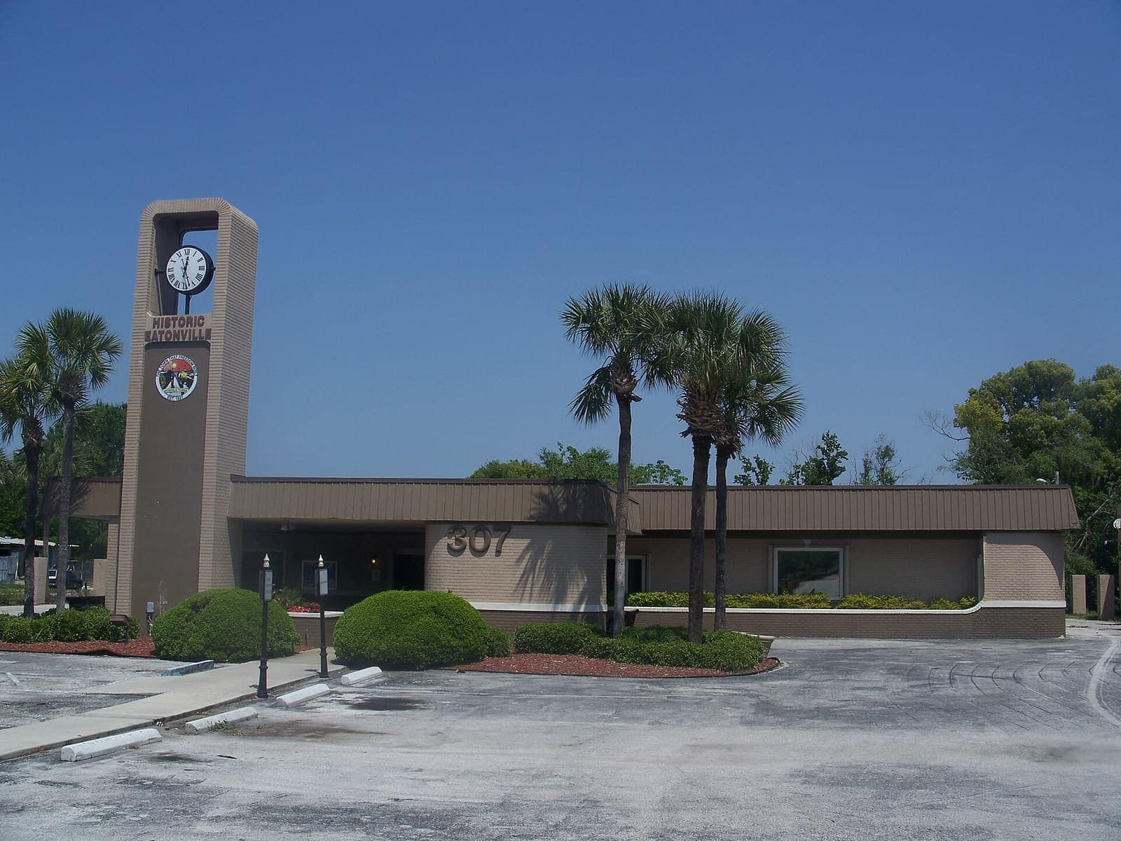 Single-storey beige town hall building with a tall clock tower under a clear blue sky.