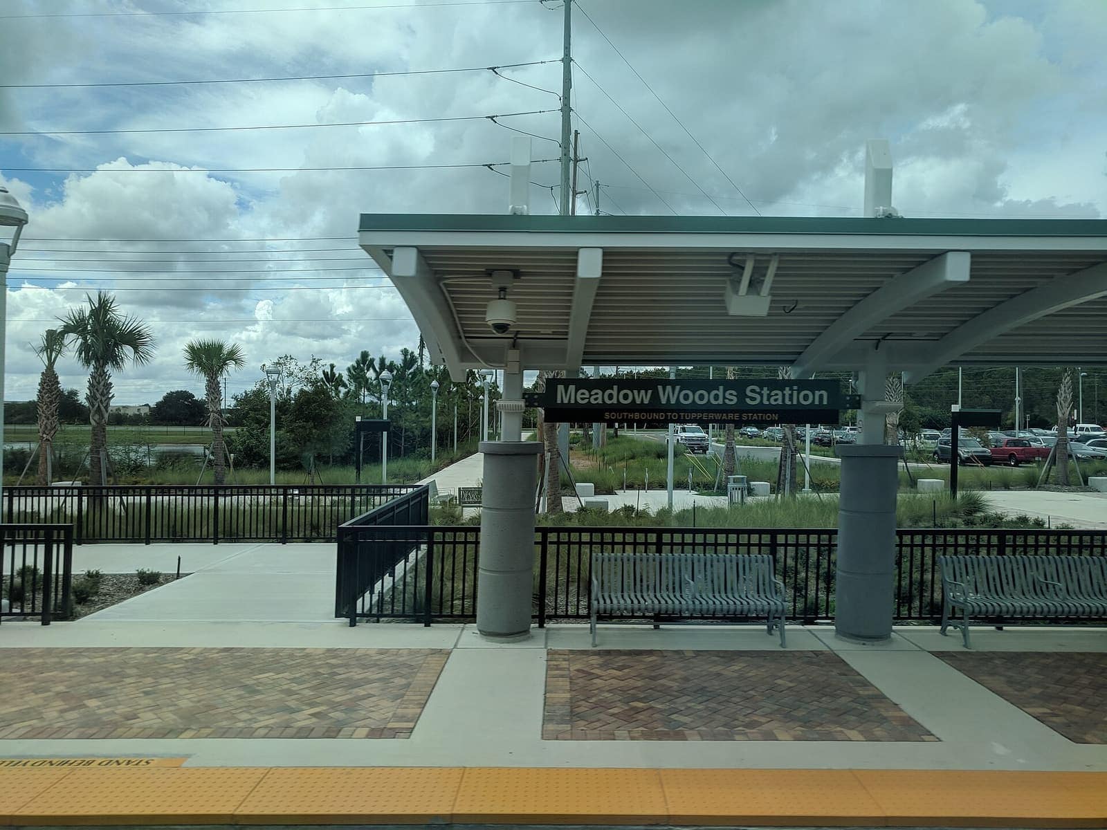 Covered SunRail platform with benches, paved walkway, and the Meadow Woods Station sign under a canopy.
