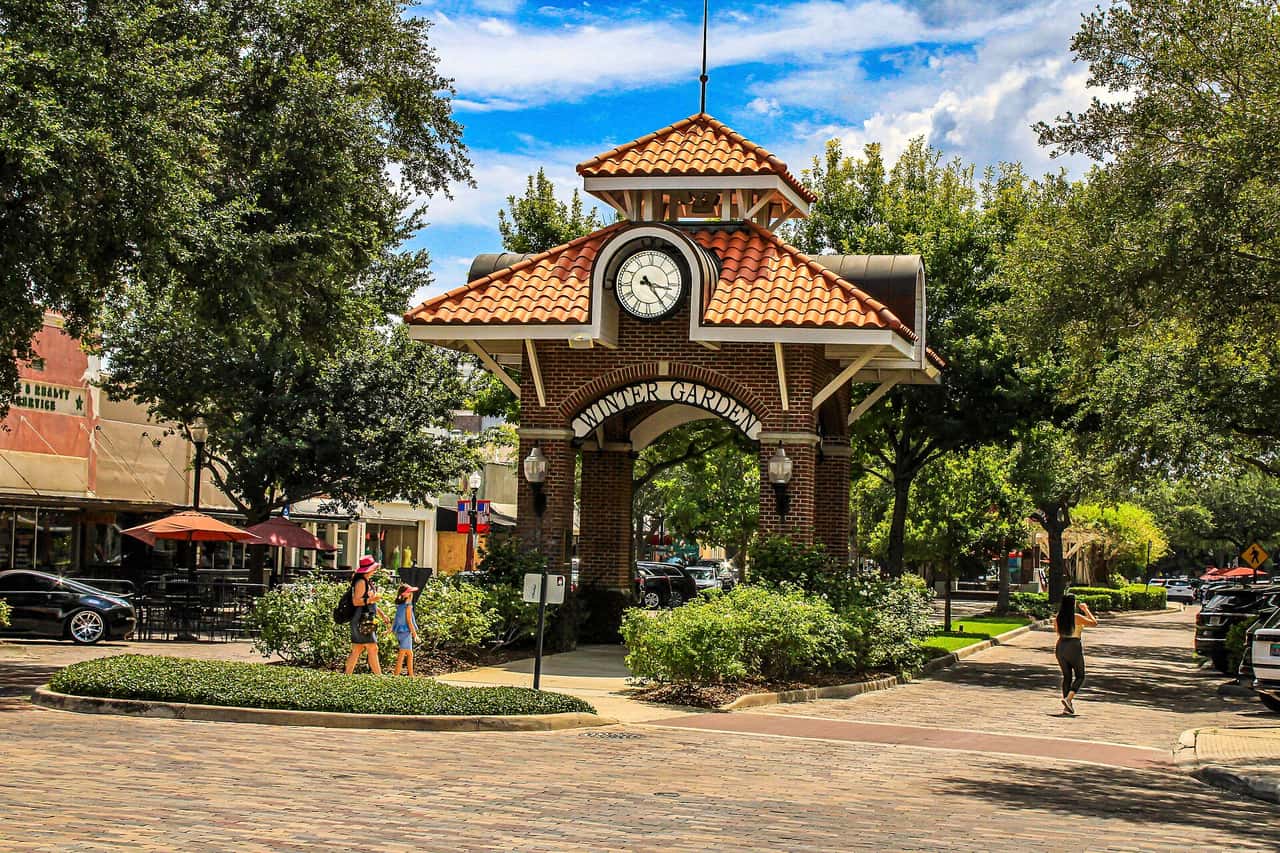 Brick clock archway with a red tiled roof stands over a paved downtown plaza on a sunny day.