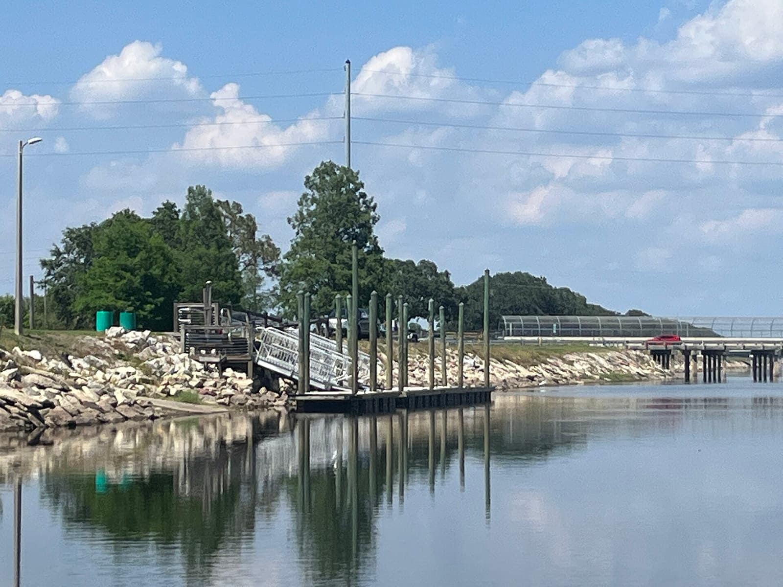 Concrete dock with metal railings and rocky embankment along a calm canal under a blue sky.