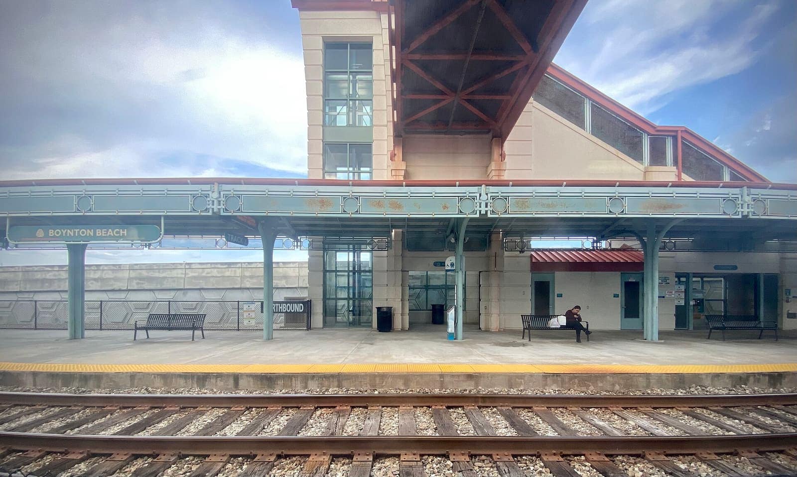 A Tri-Rail station platform with a canopy, benches and a Boynton Beach sign under a blue sky.