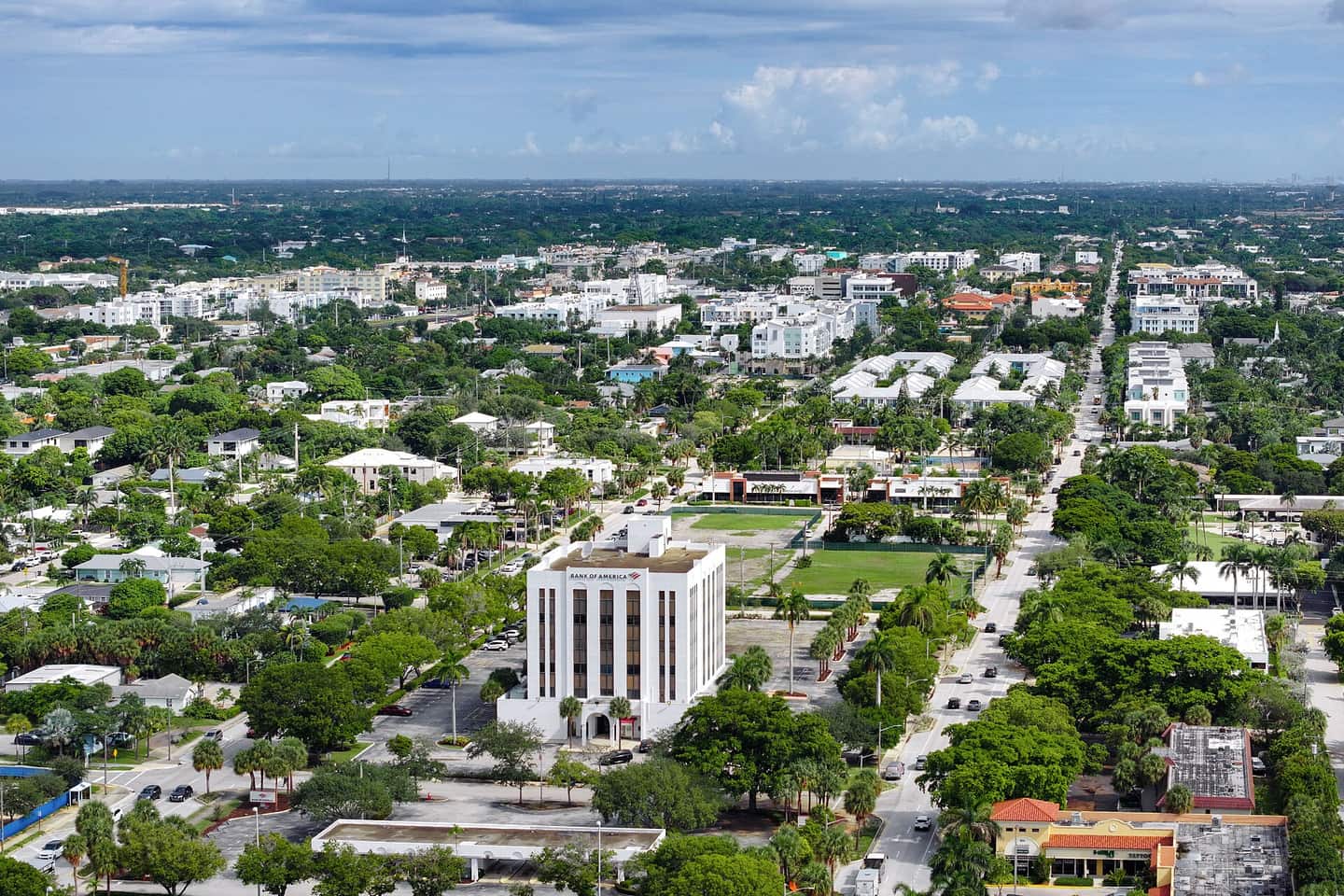 Aerial view of a low-rise city with a white office tower, green park lawns and tree-lined streets.