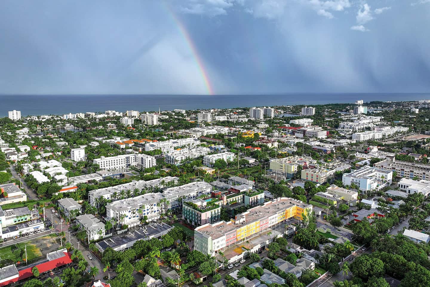 Aerial view of a coastal city with a rainbow over clouds and the Atlantic Ocean on the horizon.