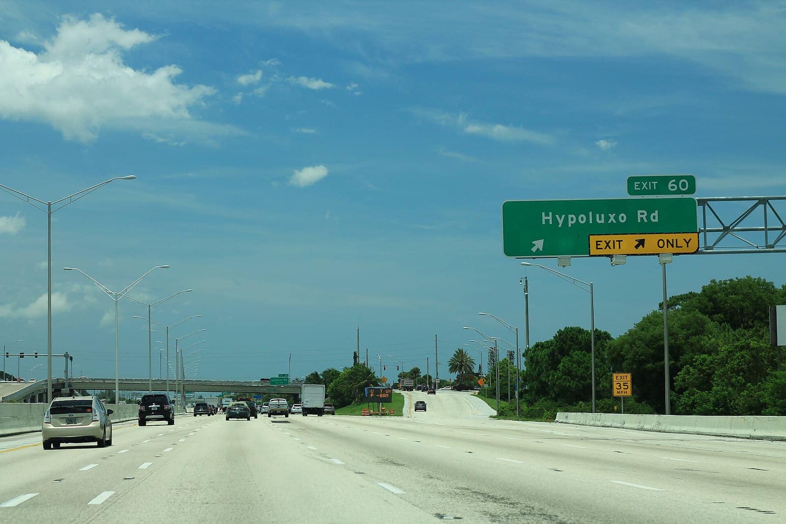 Interstate highway with a green exit sign reading Hypoluxo Rd and Exit 60, with light traffic under a blue sky.